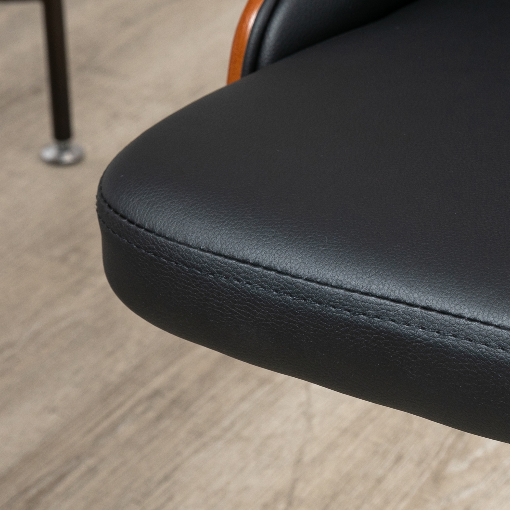 Primer plano de un asiento de cuero negro con costuras sobre suelo de madera.