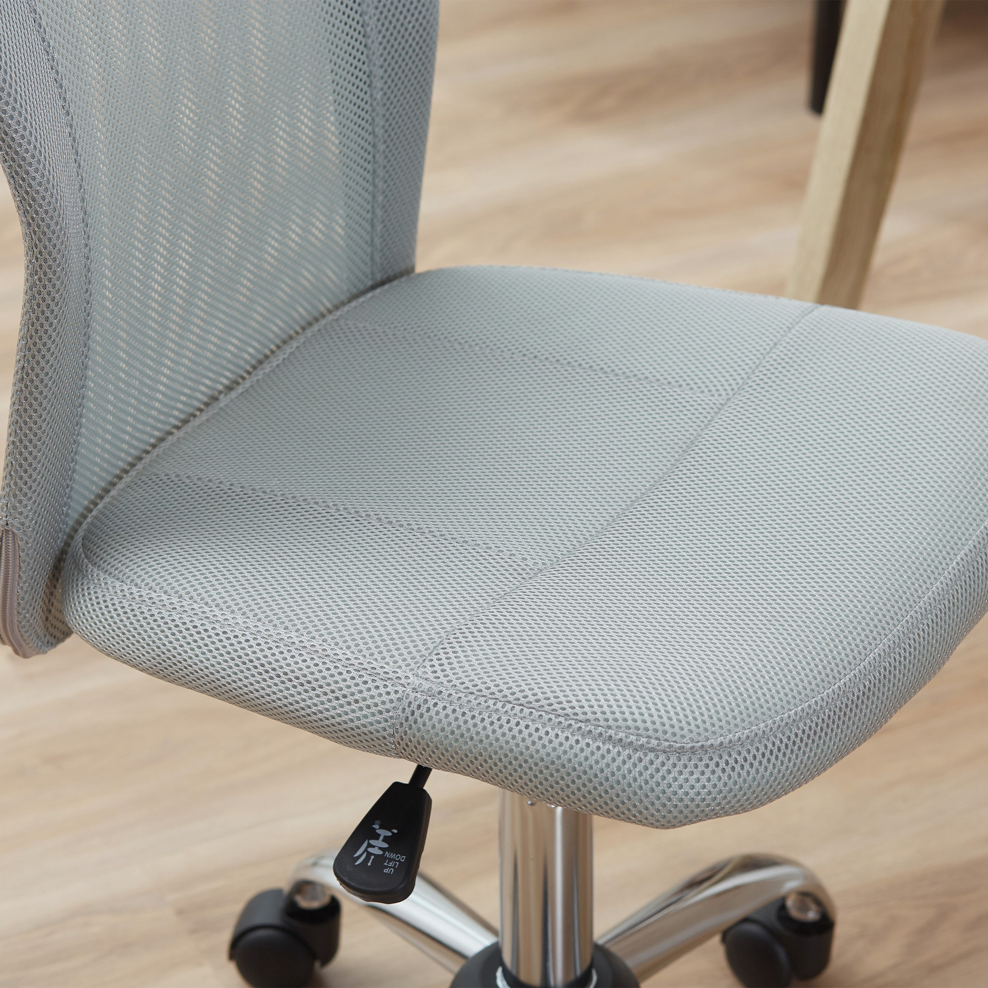 Silla de oficina de malla gris con base cromada y ruedas sobre suelo de madera.
