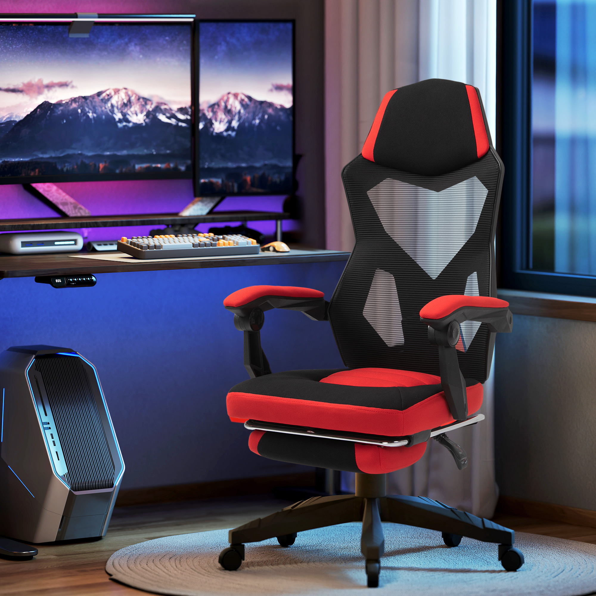 Una silla gamer roja y negra delante de un escritorio con dos monitores y un PC.