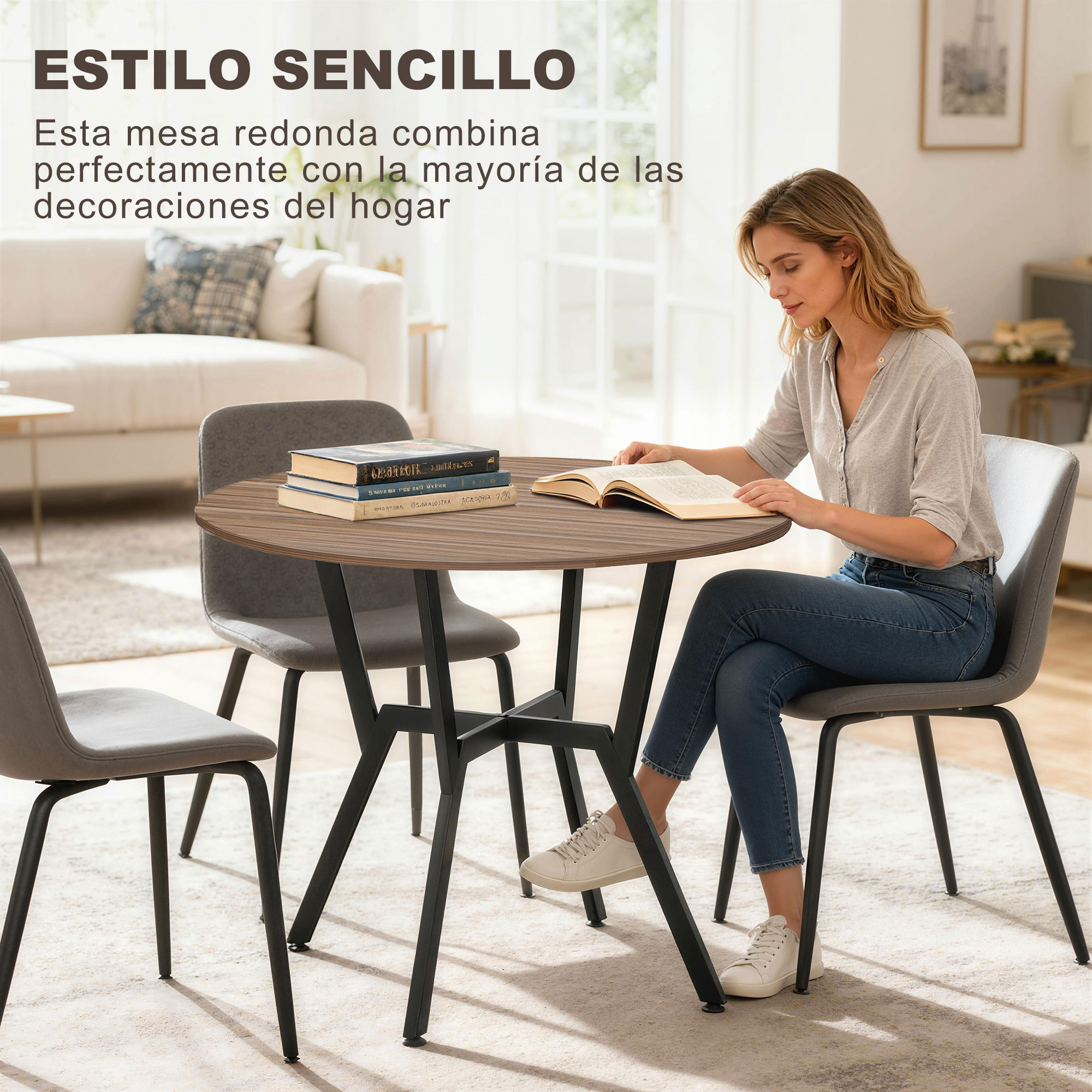 Una mujer se sienta a una mesa redonda leyendo un libro. Varios sillas y un sofá al fondo.
