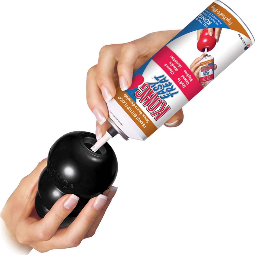 Ręka napełnia czarną zabawkę KONG smakołykiem o smaku masła orzechowego z puszki.