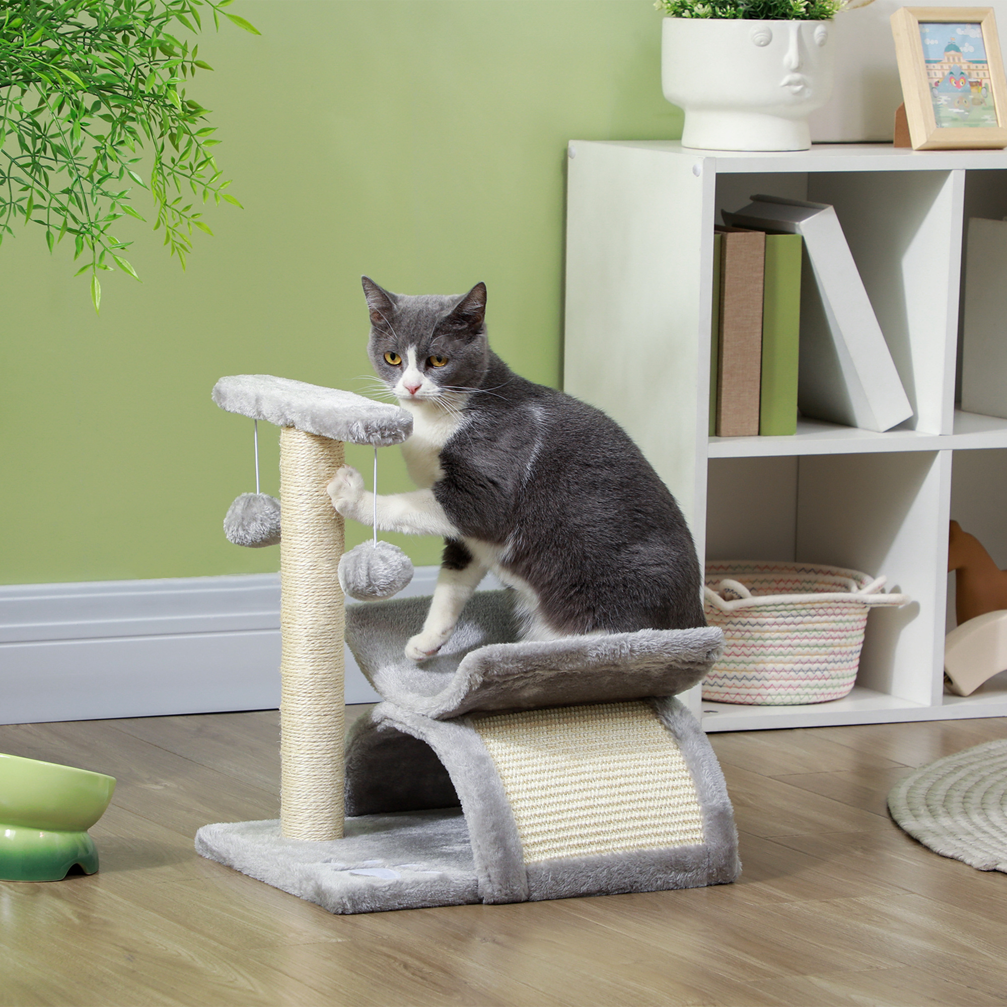 Gato gris en un árbol para gatos con juguetes y pelotas.