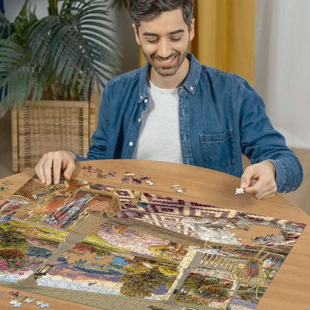 Un uomo seduto a un tavolo di legno monta un puzzle. Tiene in mano un pezzo.
