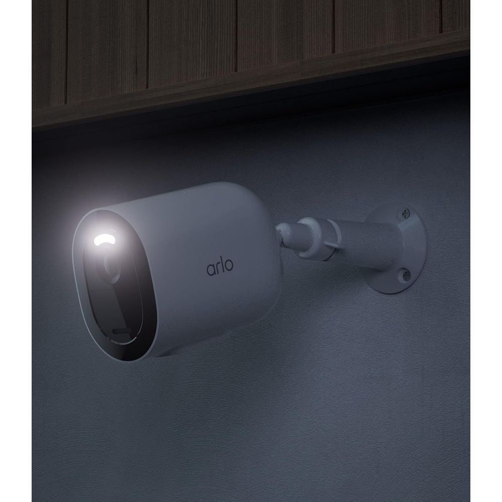 Una telecamera Arlo bianca con obiettivo illuminato, montata su un muro di notte.
