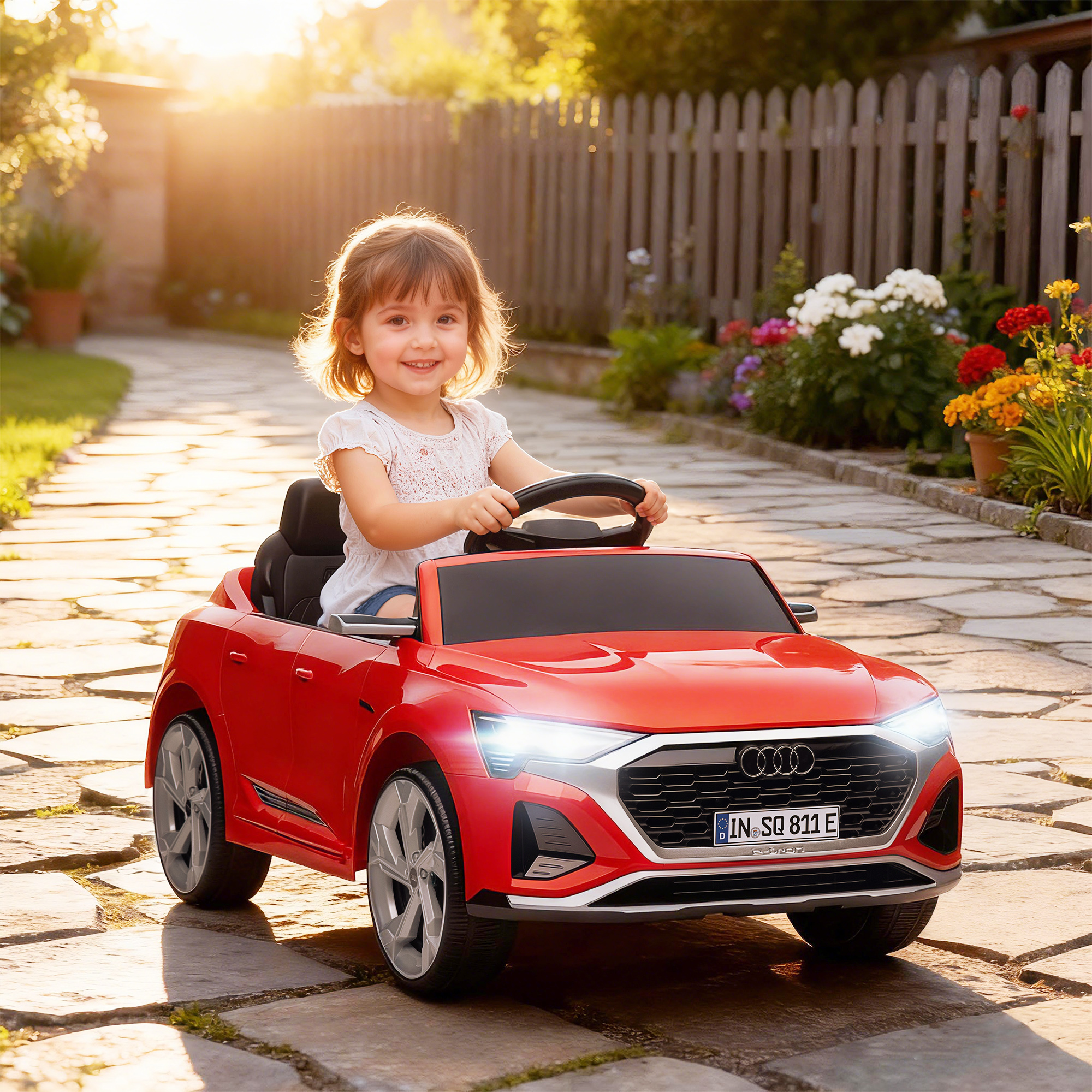 Una niña conduce un coche de juguete rojo en un jardín.