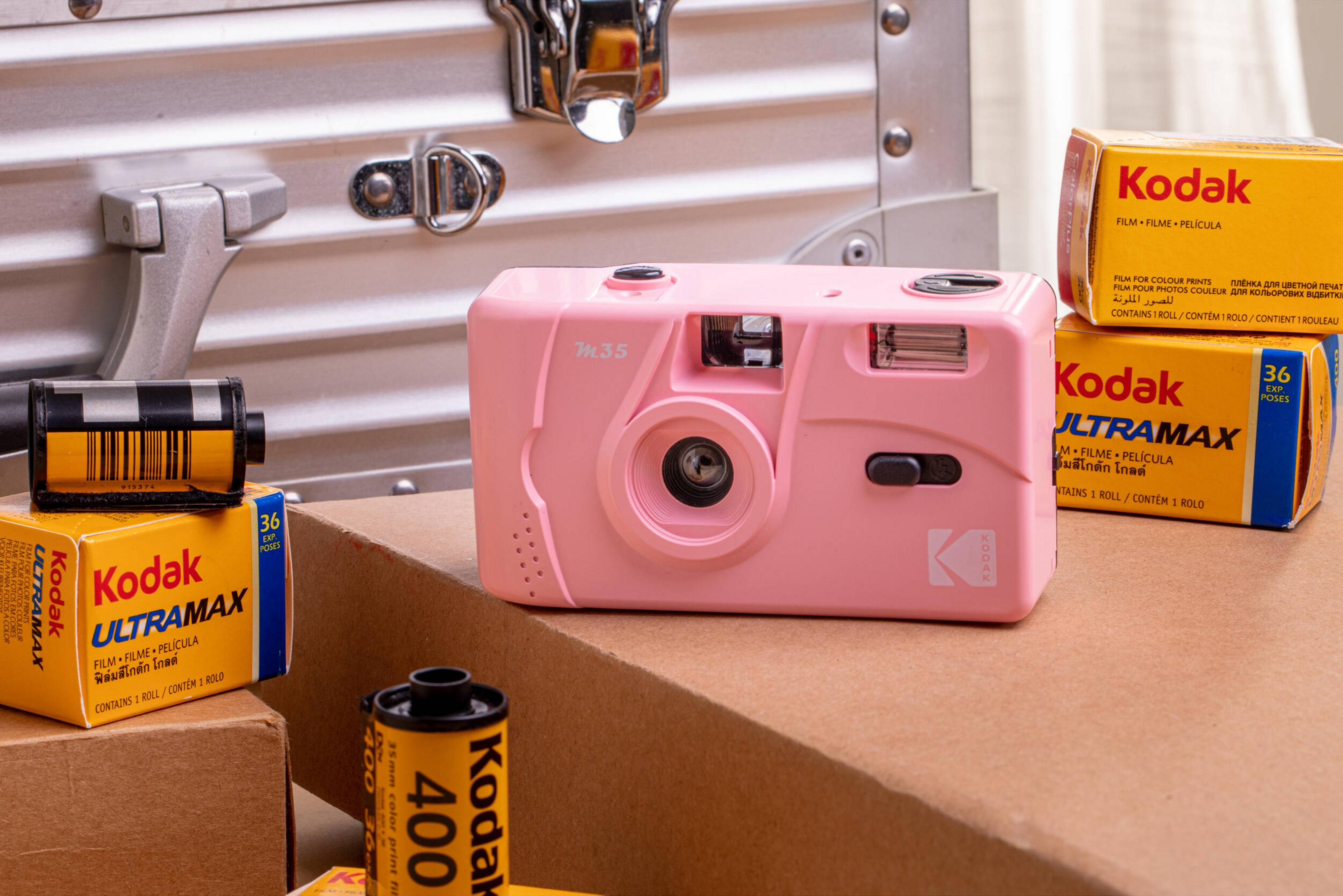 Eine rosafarbene Einwegkamera mit Kodak-Filmpackungen und einer silbernen Metallbox.