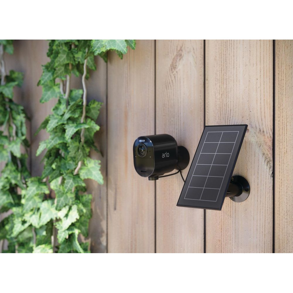 Eine schwarze Arlo-Überwachungskamera mit Solarpanel an einer Holzwand.