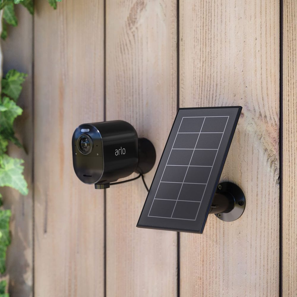 Schwarze Arlo-Kamera und Solarpanel an Holzfassade montiert.