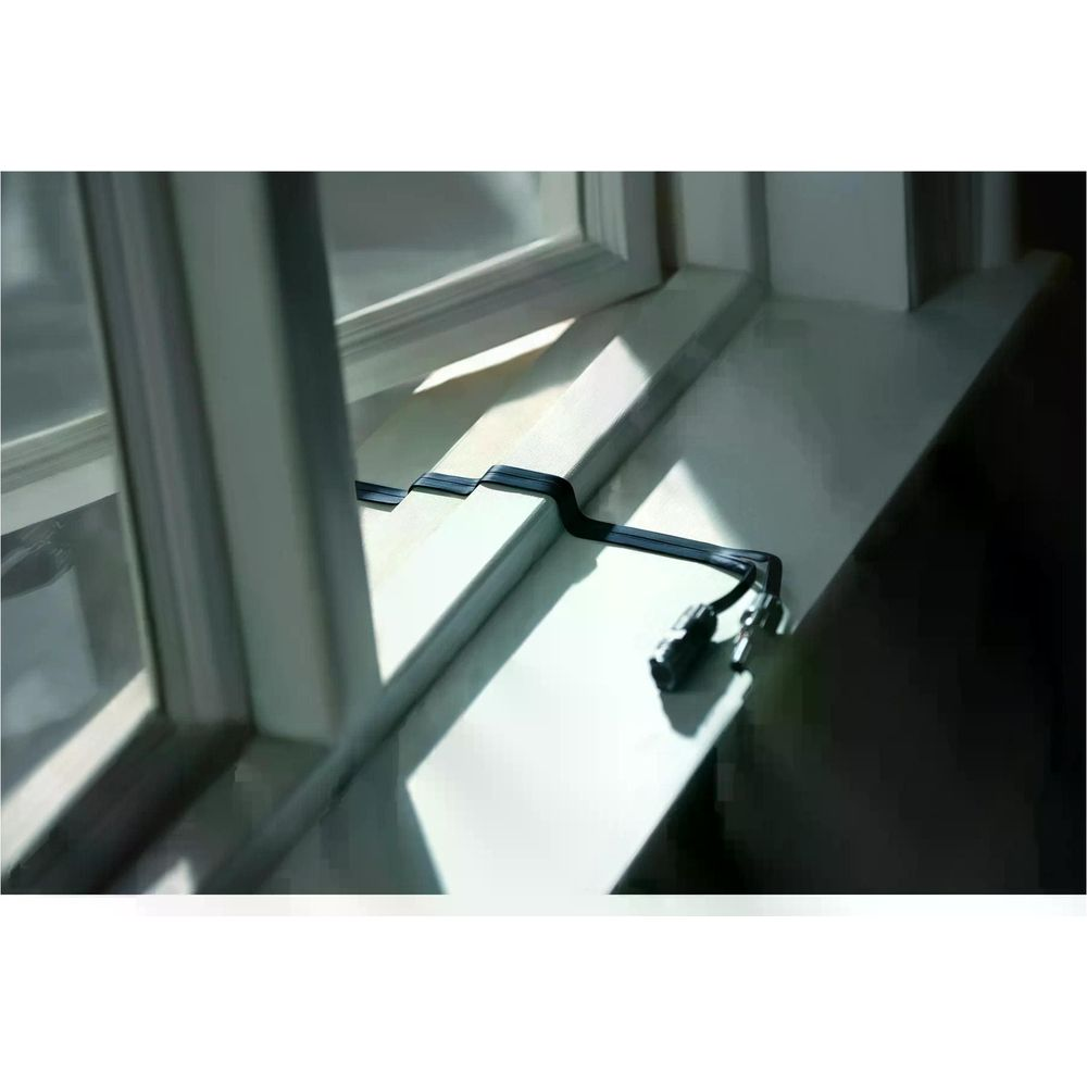 Czarny kabel wijący się po białym parapecie z promieniami słońca.