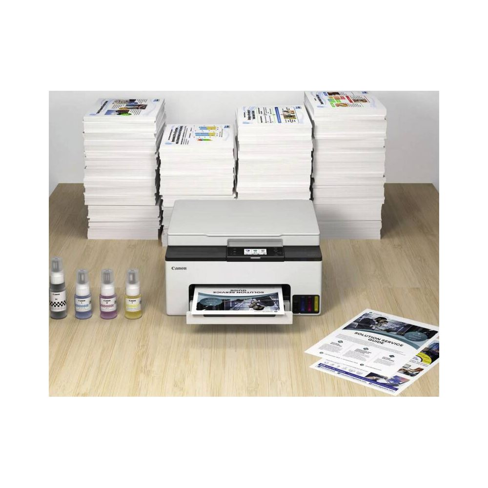 Drukarka Canon z czterema butelkami tuszu i stosami papieru.