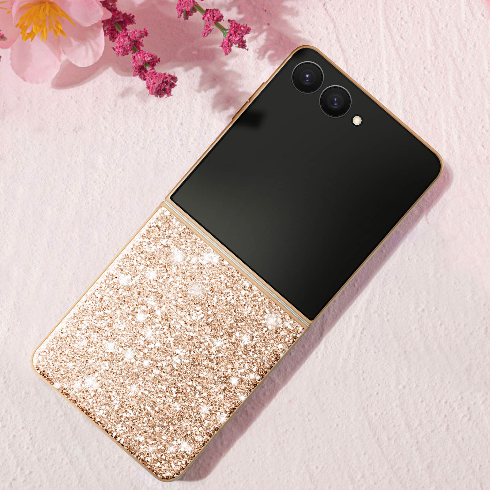 Gouden vouwtelefoon met glitterrug en zwart scherm naast roze bloemen.