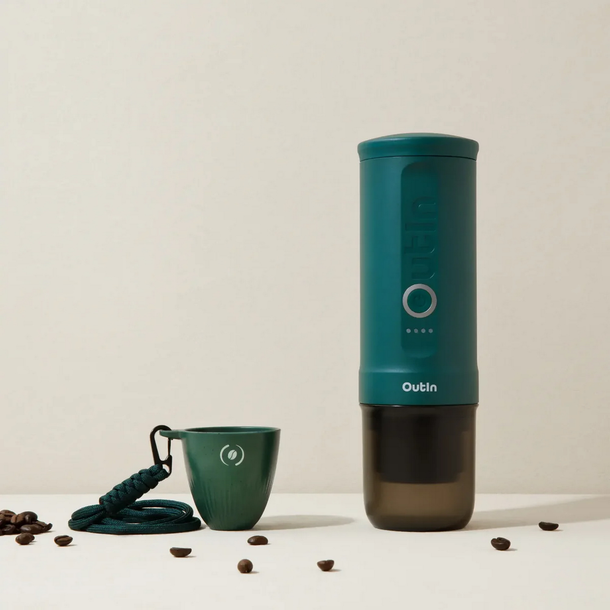 Una caffettiera verde con tazza e chicchi su sfondo chiaro.