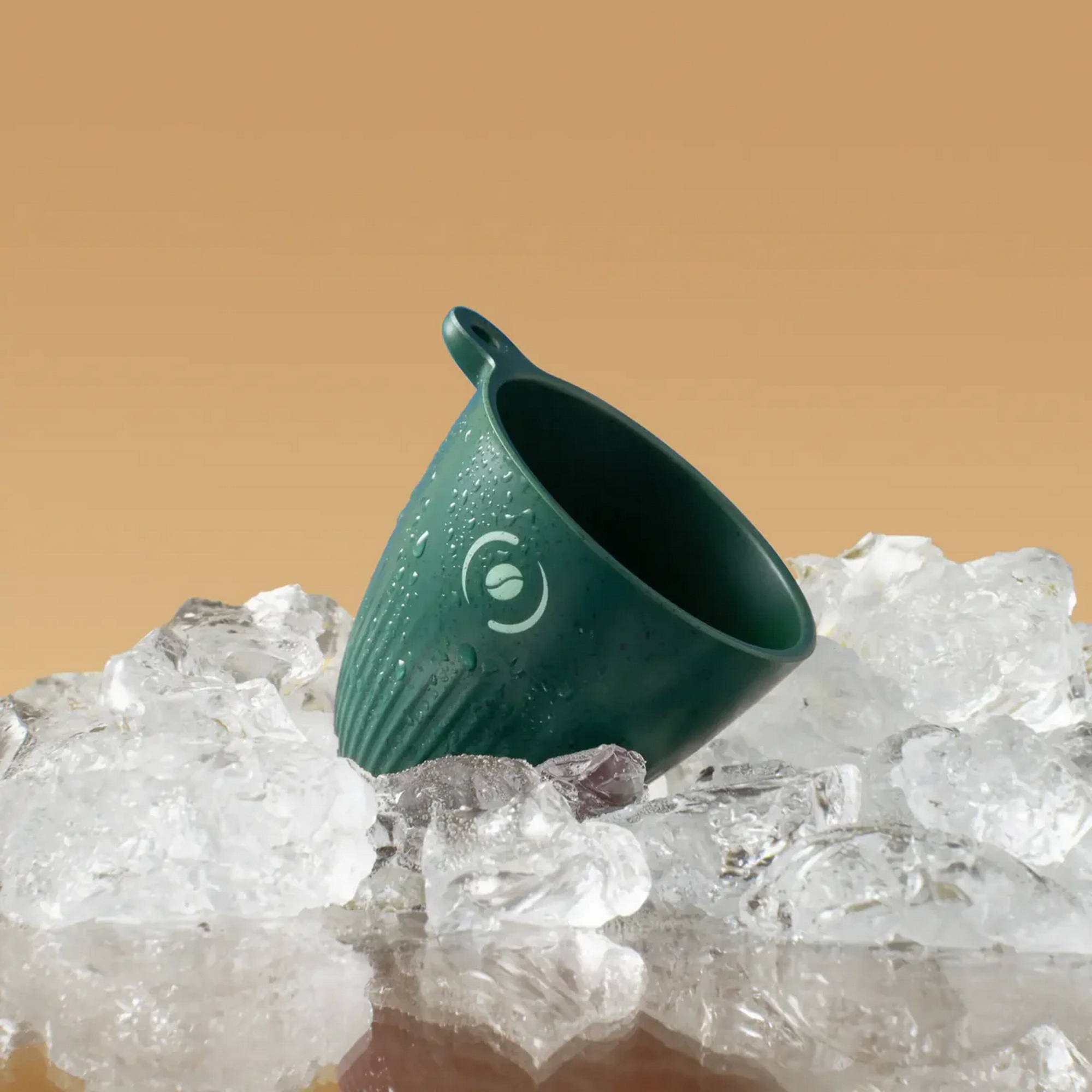 Una tazza verde con gocce d'acqua poggia su cubetti di ghiaccio.