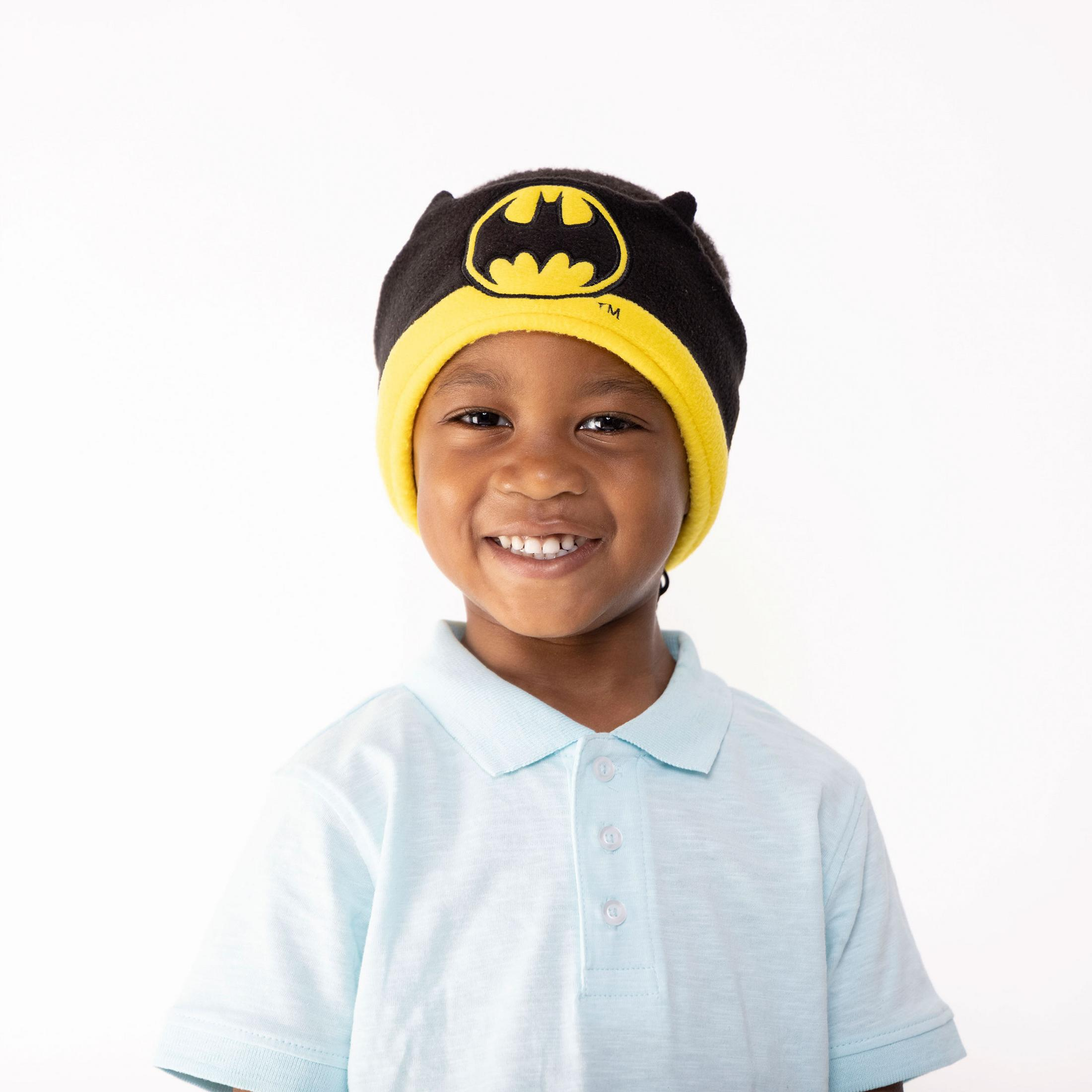 Un ragazzo sorride, indossa un cappello di Batman e una polo azzurra.