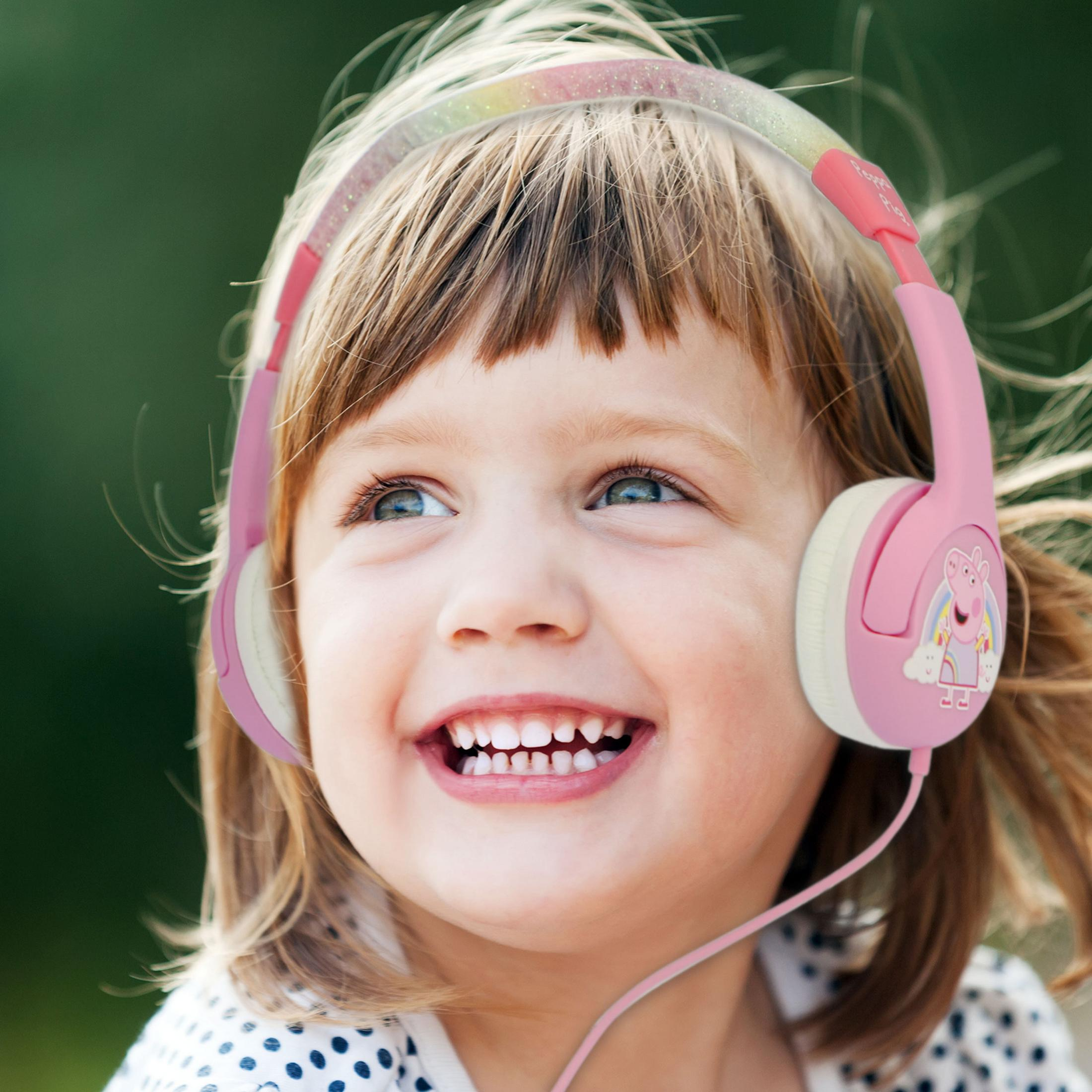 Uśmiechnięta dziewczynka w różowych słuchawkach Peppa Pig na zewnątrz.