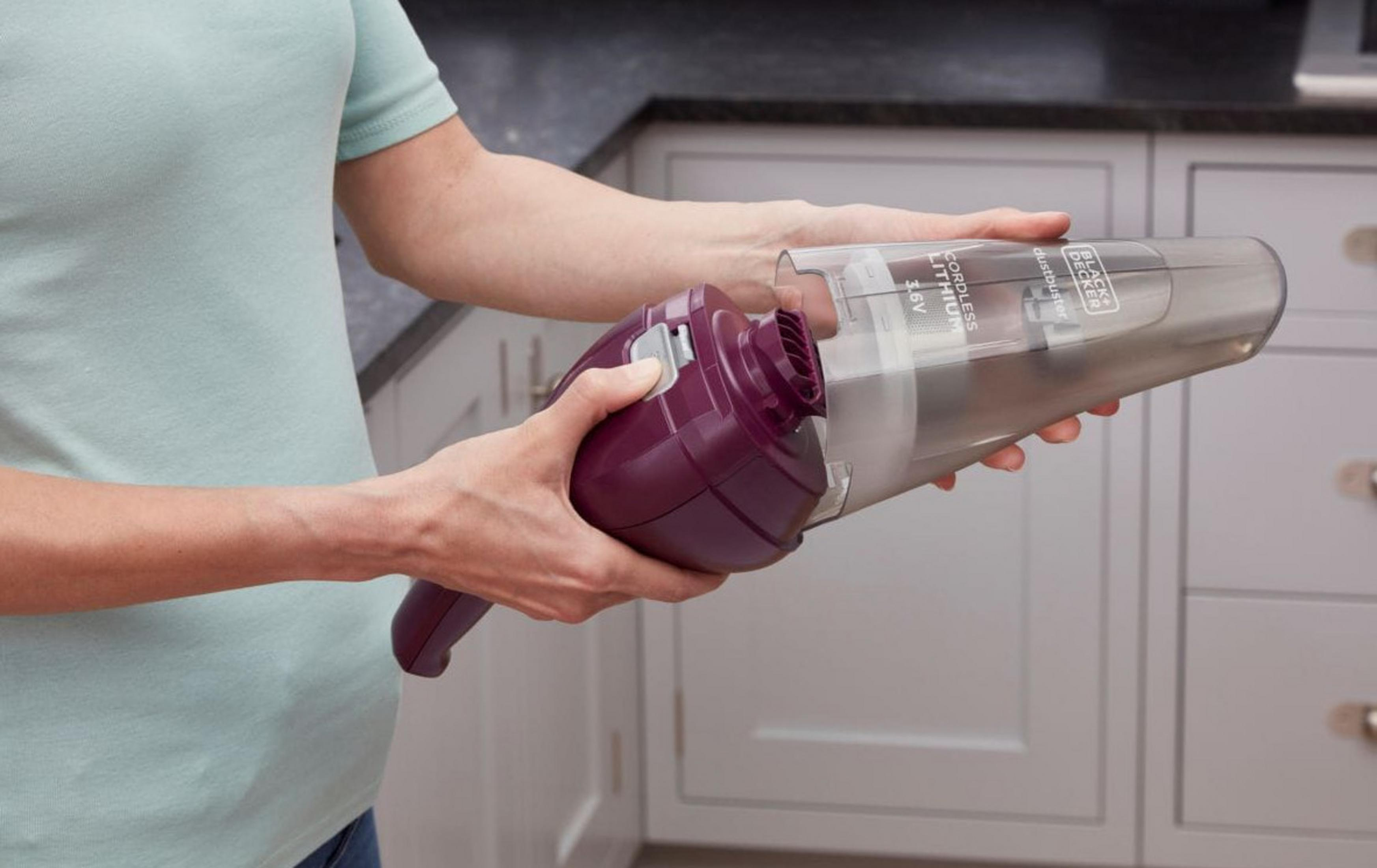 Osoba trzyma ręczny odkurzacz z fioletowym uchwytem i przezroczystym pojemnikiem.