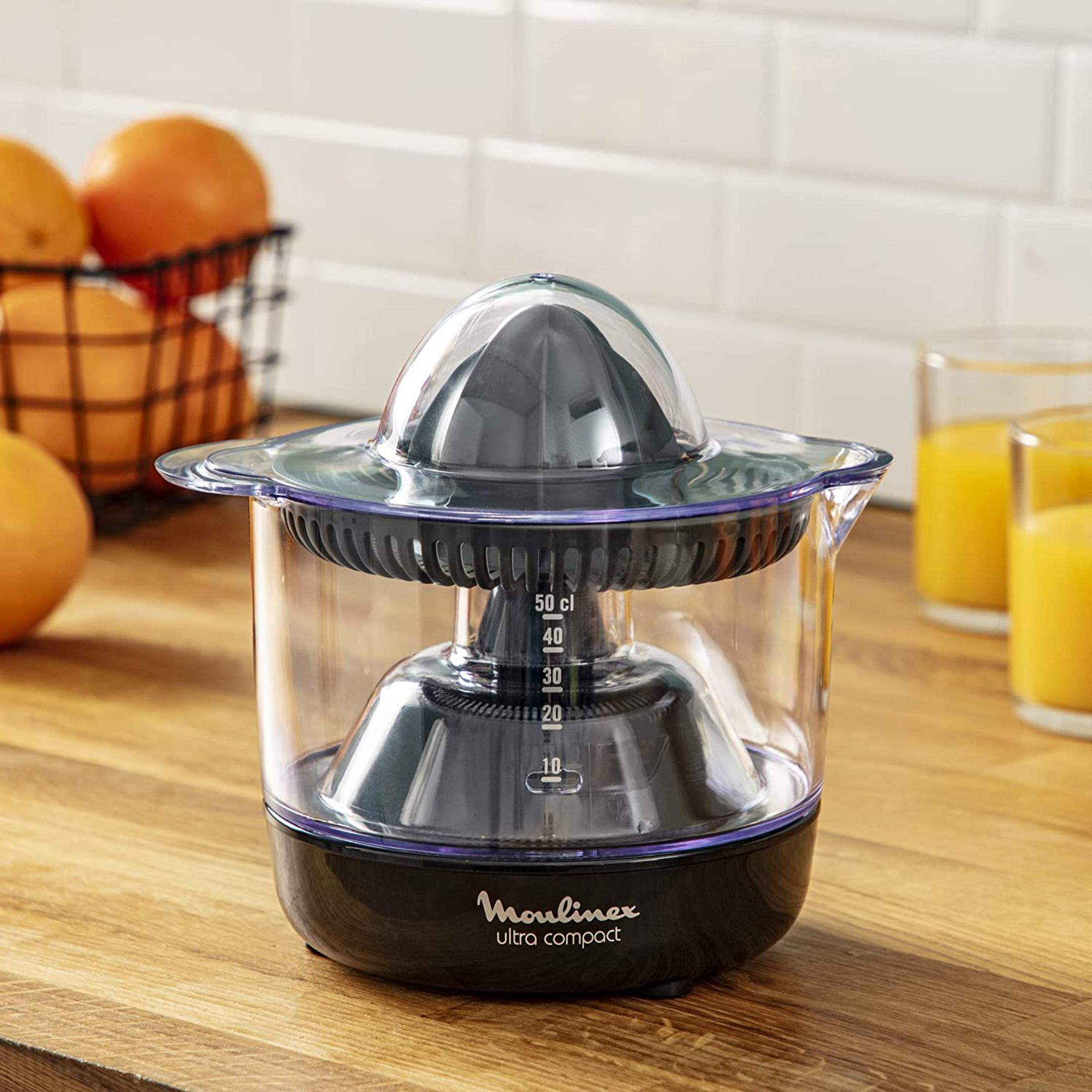 Elektryczna wyciskarka do cytrusów z miarką i pomarańczami w tle.