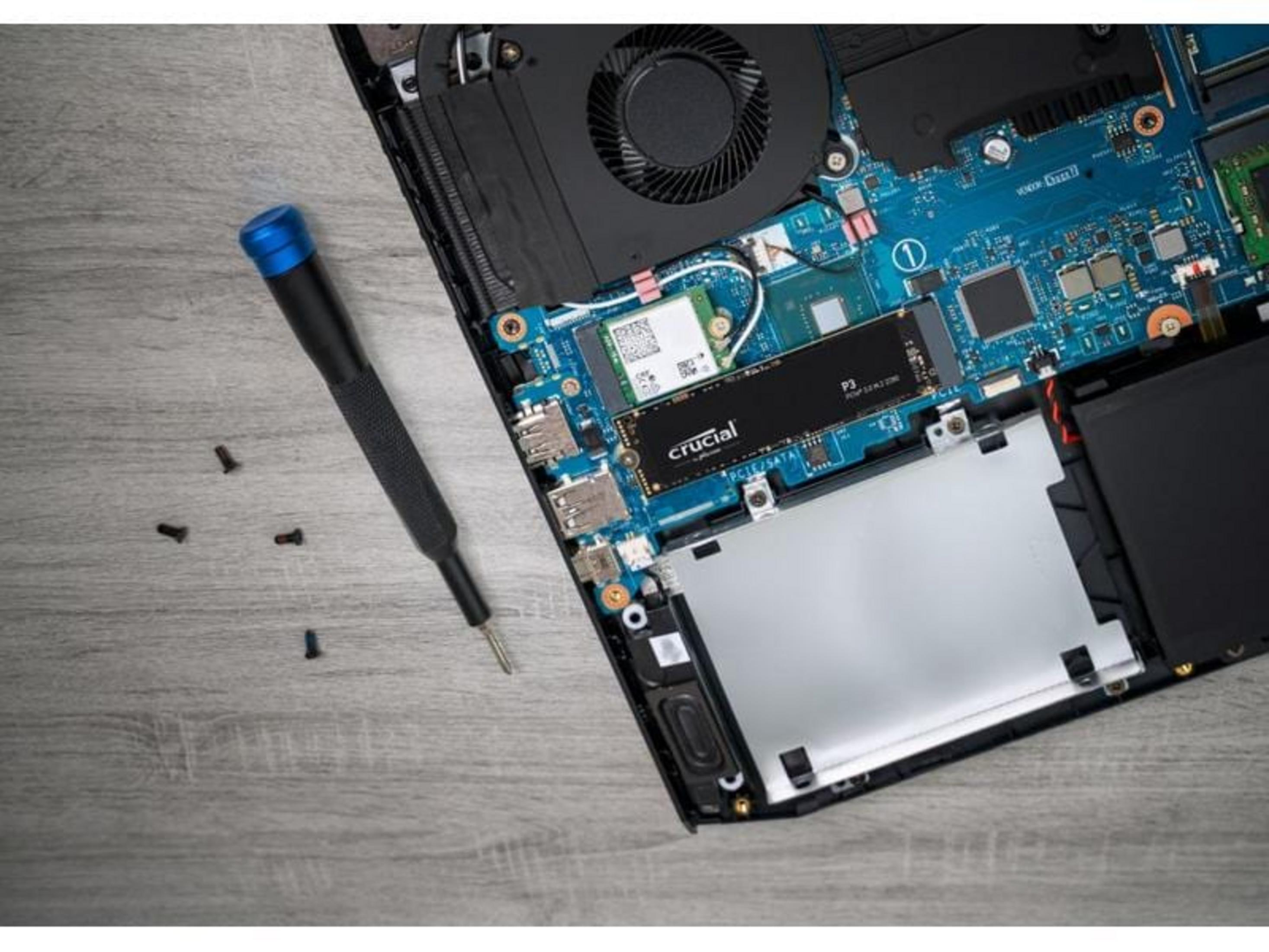 Śrubokręt obok otwartego laptopa z płytą główną, wentylatorem i dyskiem SSD.
