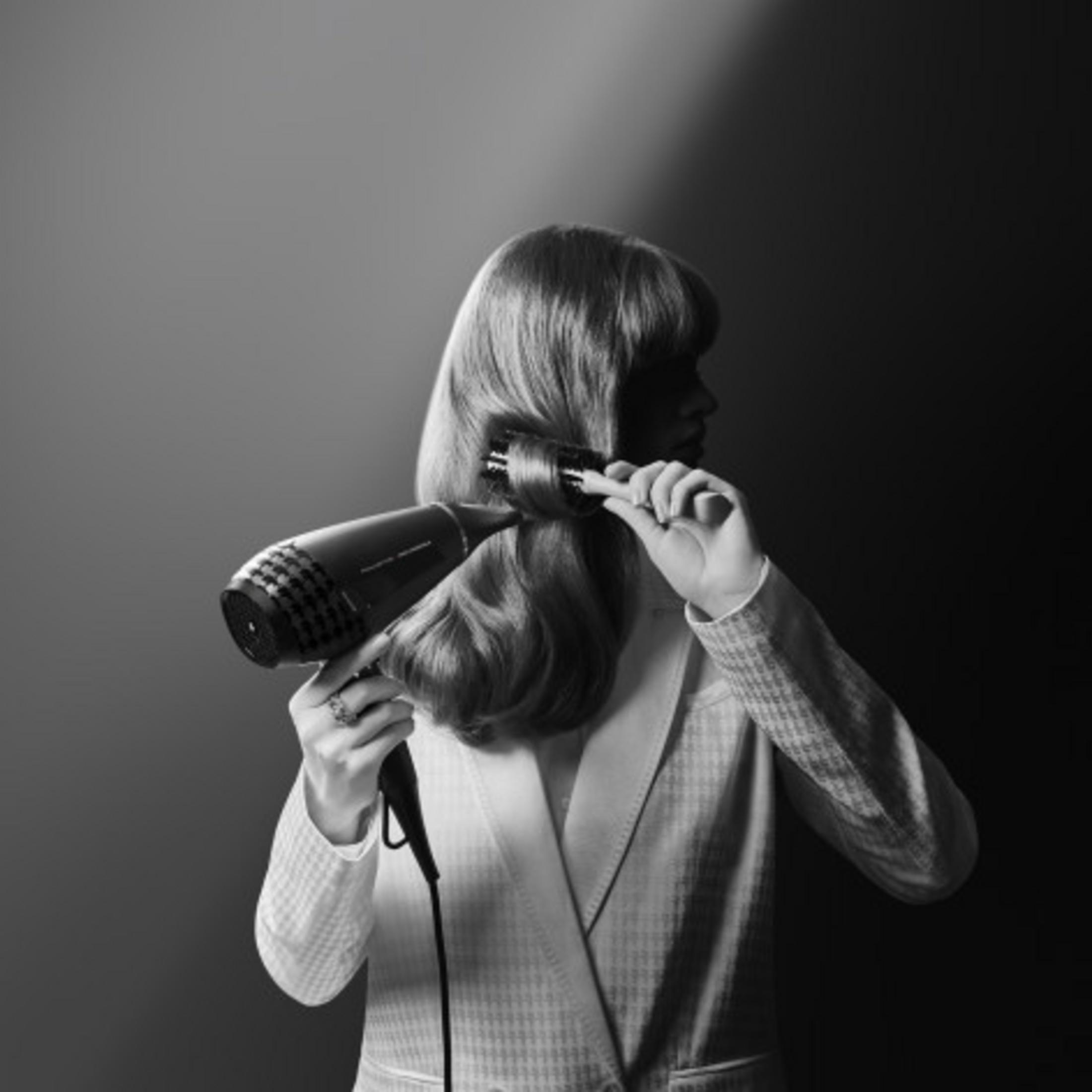 Kobieta stylizuje blond włosy suszarką i okrągłą szczotką.