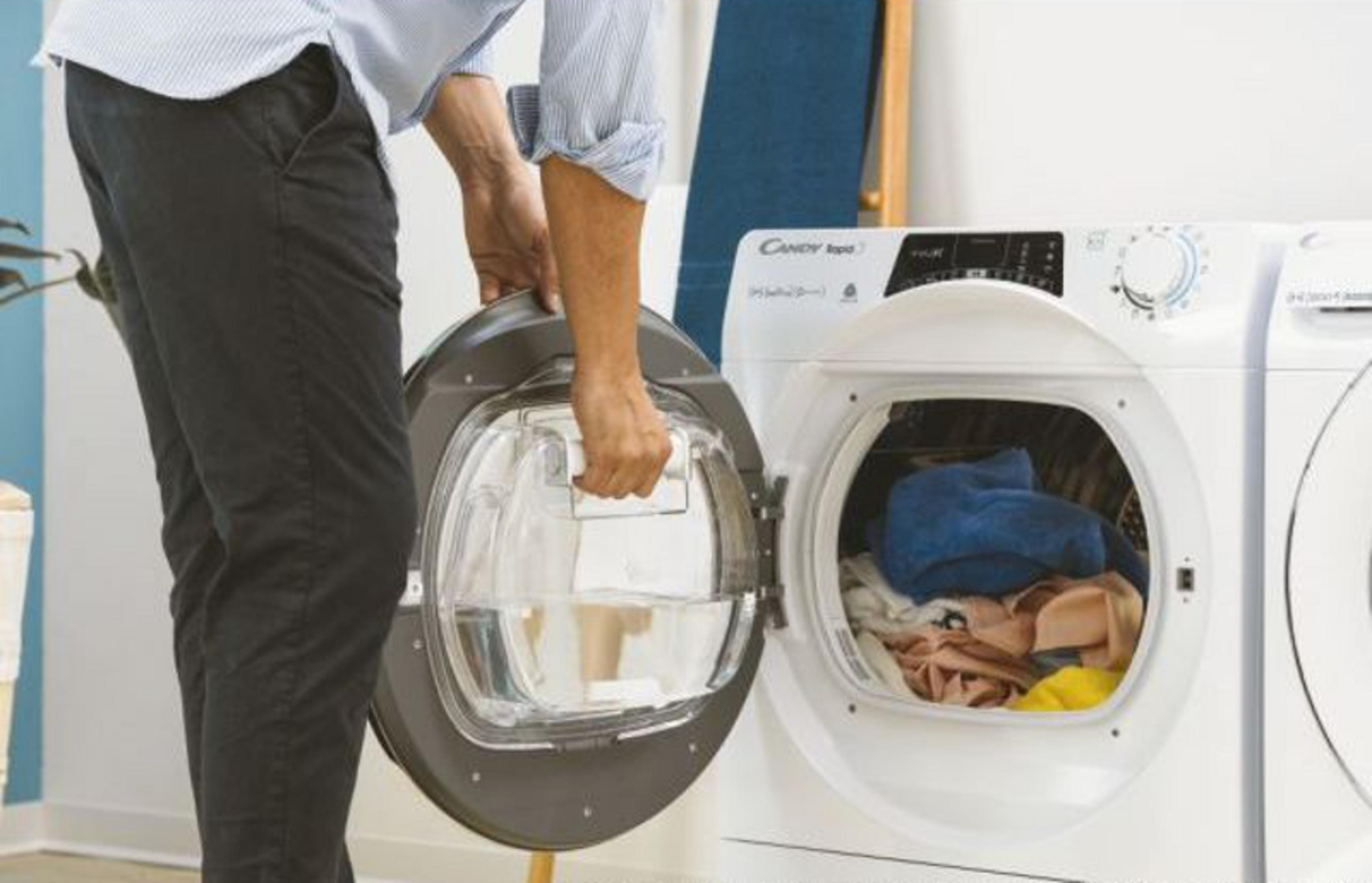 Una persona apre l'oblò di una lavatrice con vestiti all'interno.