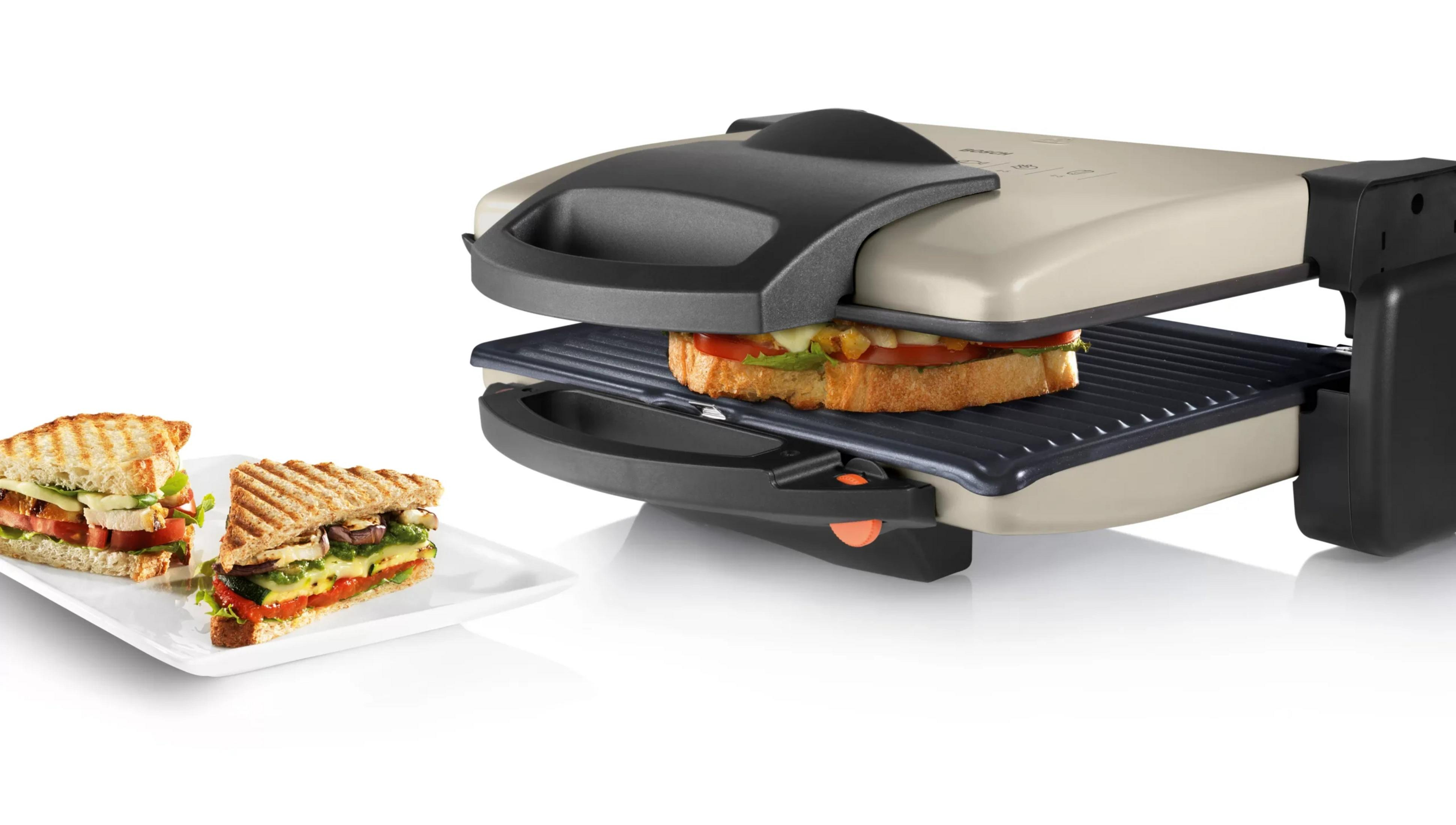 Tostapane per sandwich con un sandwich dentro e due su un piatto.