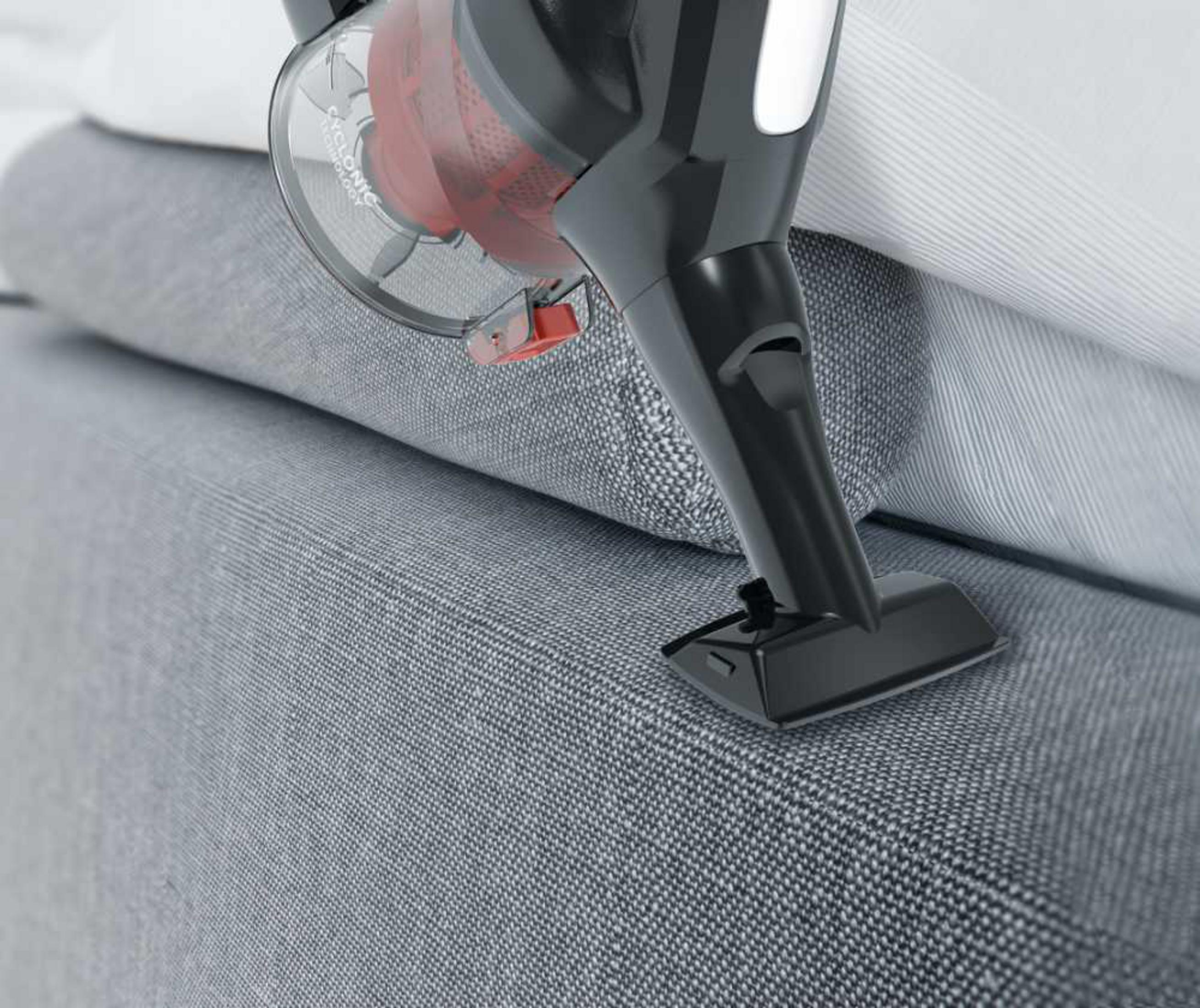 Un aspirapolvere portatile nero pulisce un divano grigio con biancheria da letto a righe bianche.