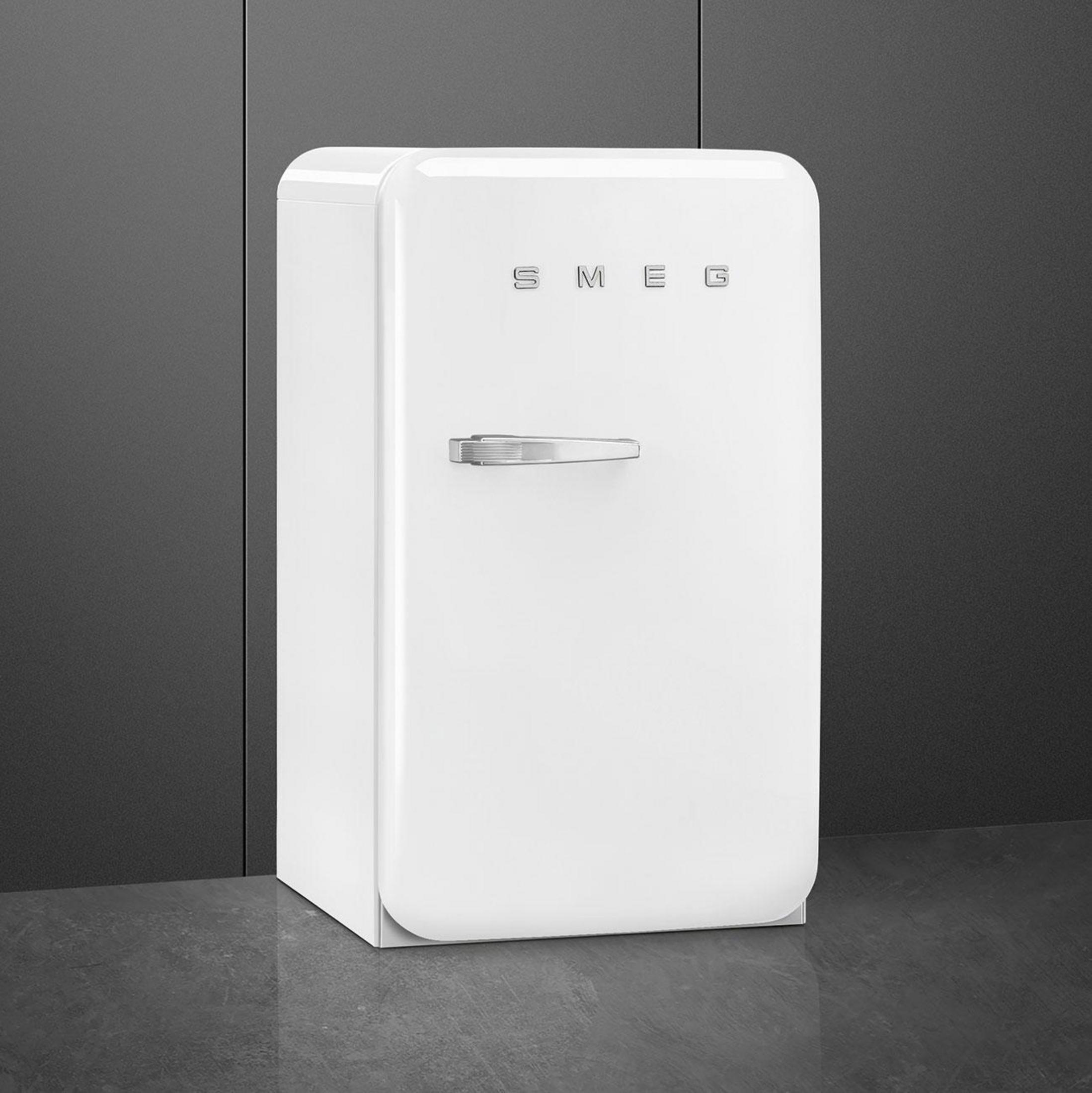 Un refrigerador blanco con asa cromada está sobre un suelo oscuro.