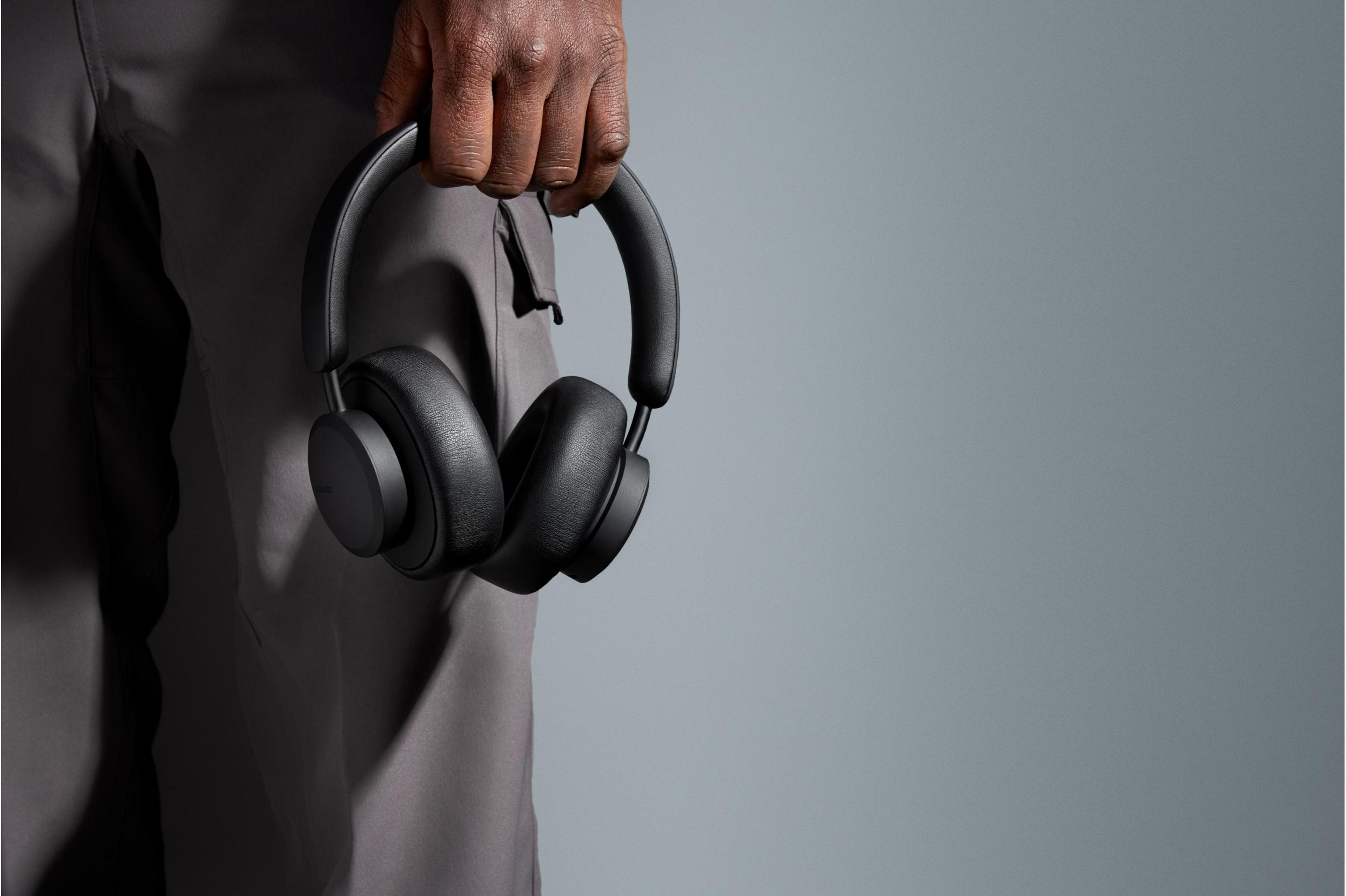 Osoba trzyma czarne słuchawki na tle szarości.