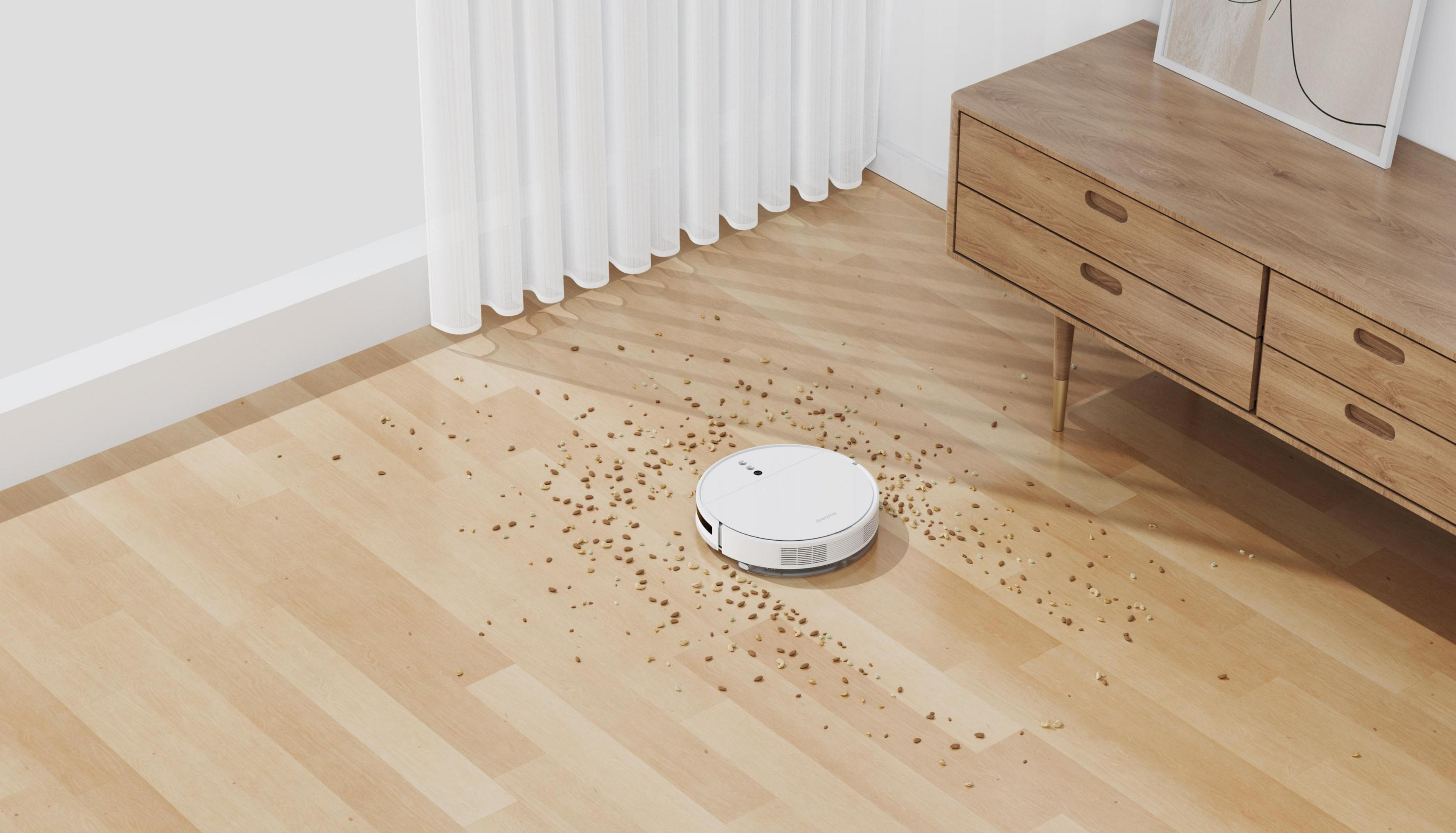 Un robot aspirador blanco limpia un suelo de madera con escombros.