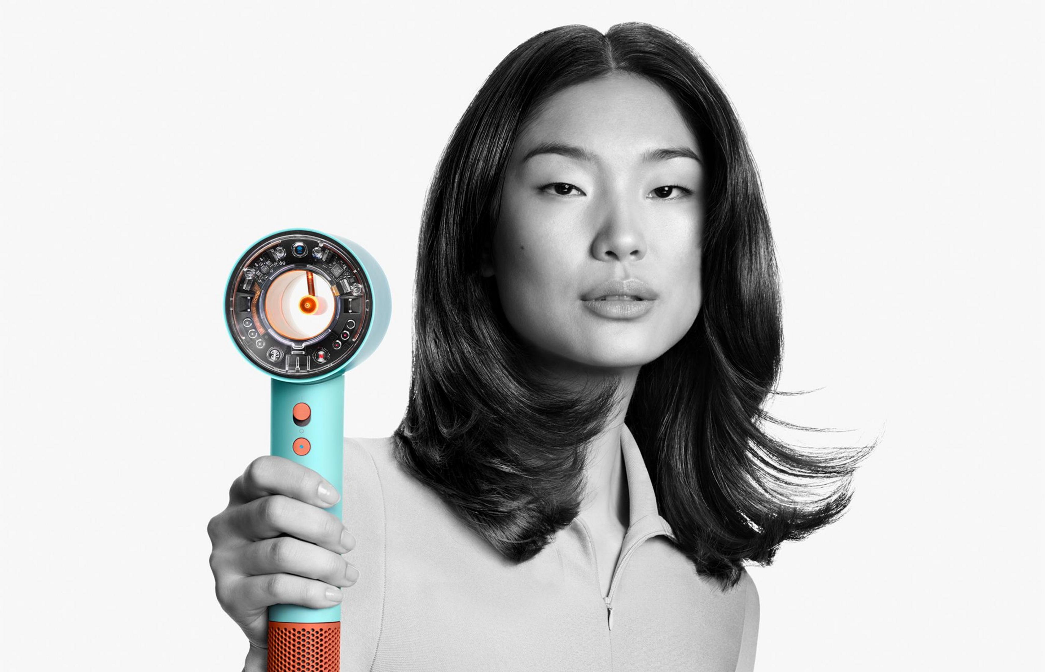 Eine Frau hält einen türkisfarbenen Haartrockner mit orangen Akzenten, dessen Inneres sichtbar ist.