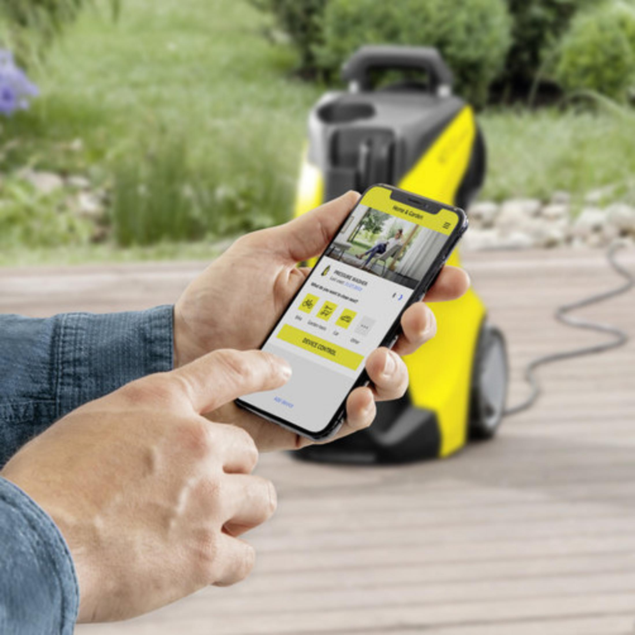 Una mano tiene uno smartphone con un'app per idropulitrice, accanto a una macchina gialla.