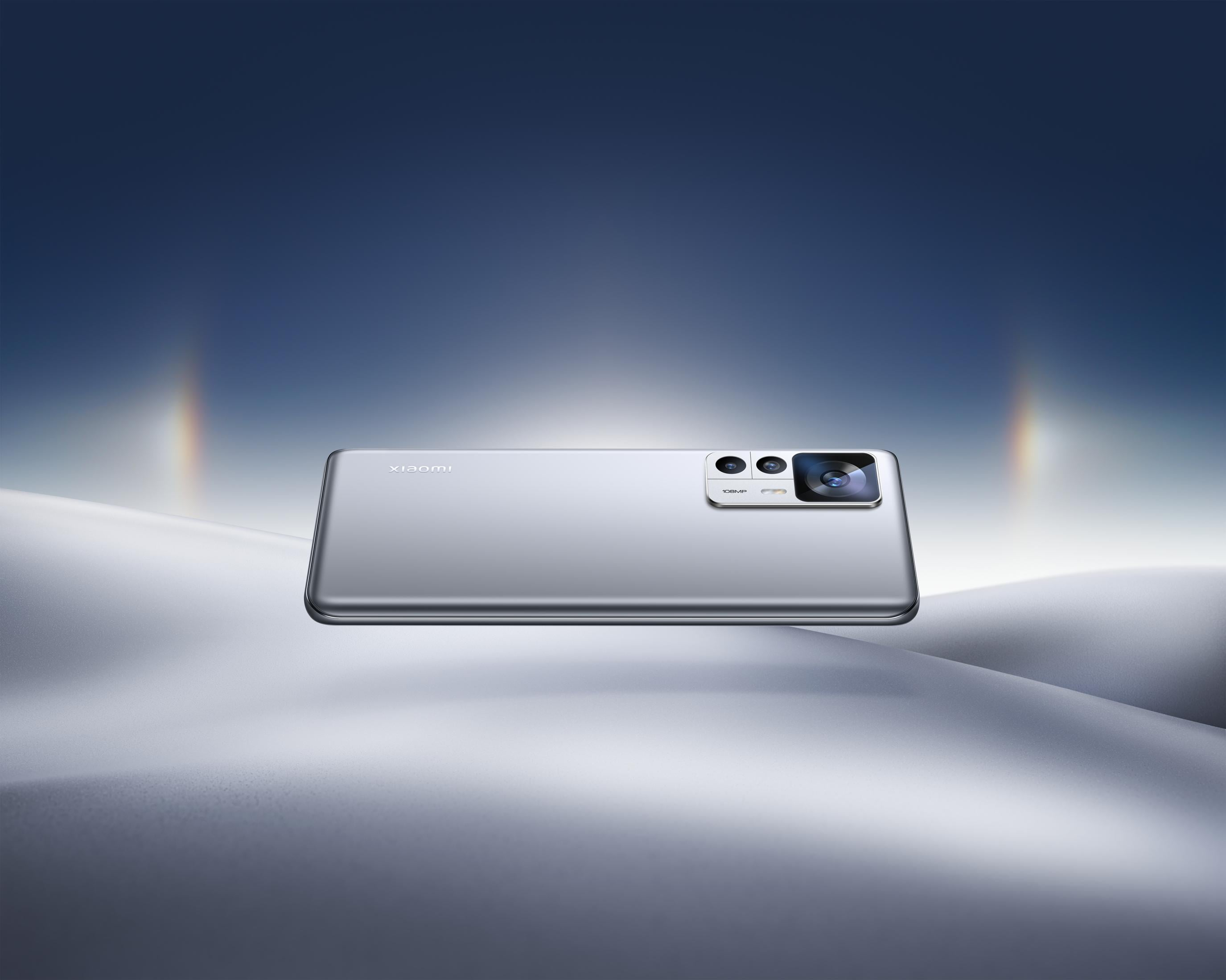 Ein silbernes Smartphone mit drei Kameras liegt auf einer weichen, weißen Oberfläche.