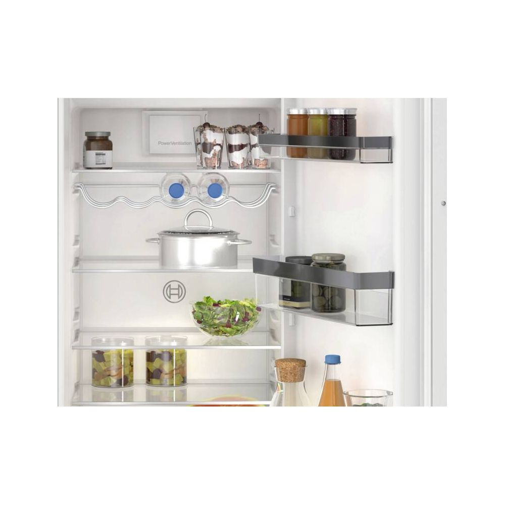 Otwarta lodówka z słoikami, miską sałatki, garnkiem i butelkami.