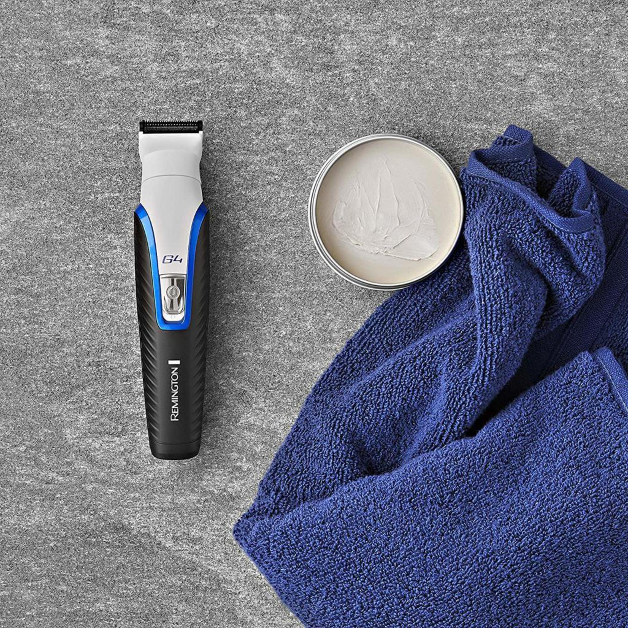 Ein weißer und blauer Remington Trimmer liegt neben einer Salbe und einem blauen Handtuch.