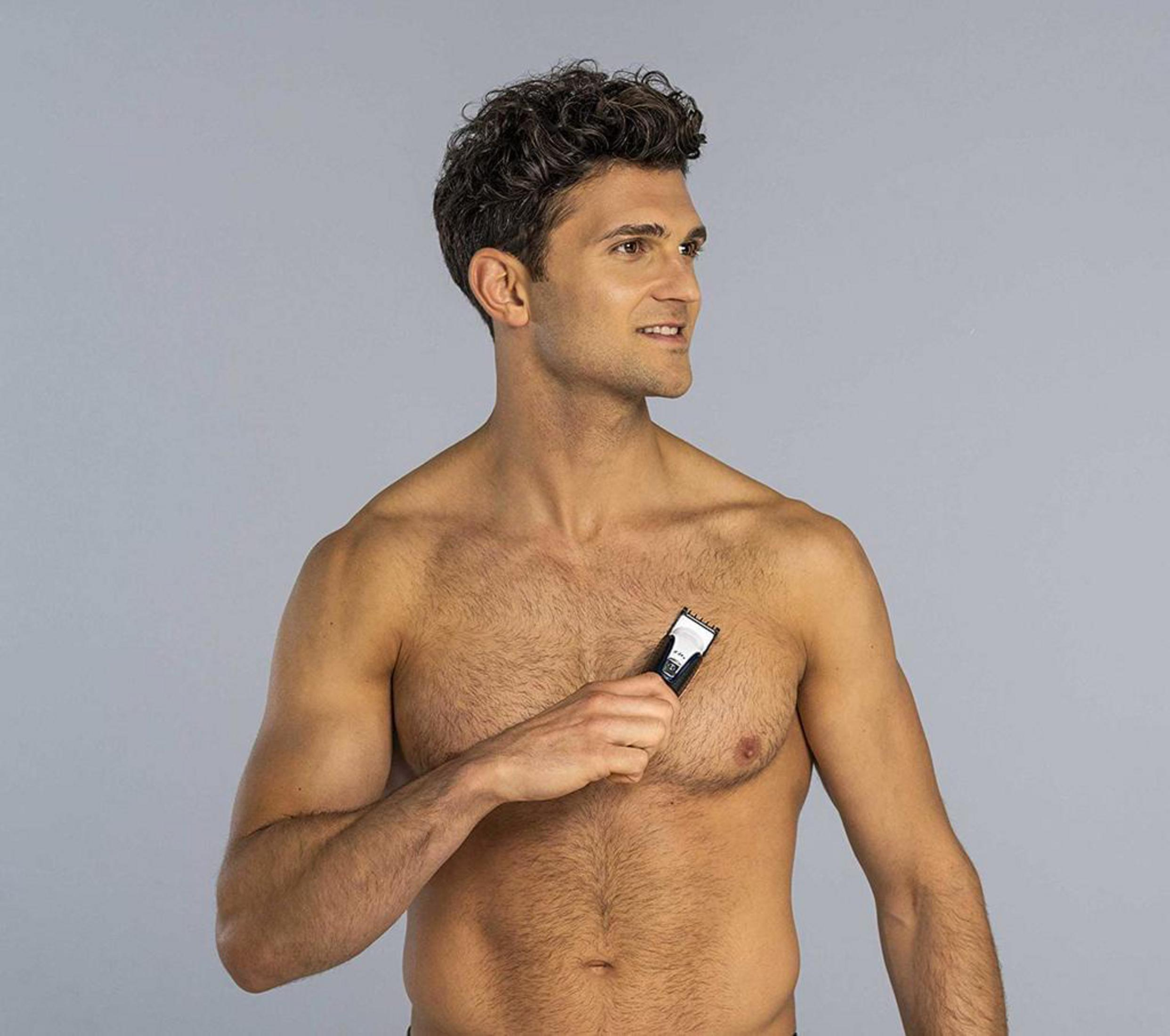 Ein Mann mit dunklen Haaren benutzt einen Trimmer auf seiner Brust.