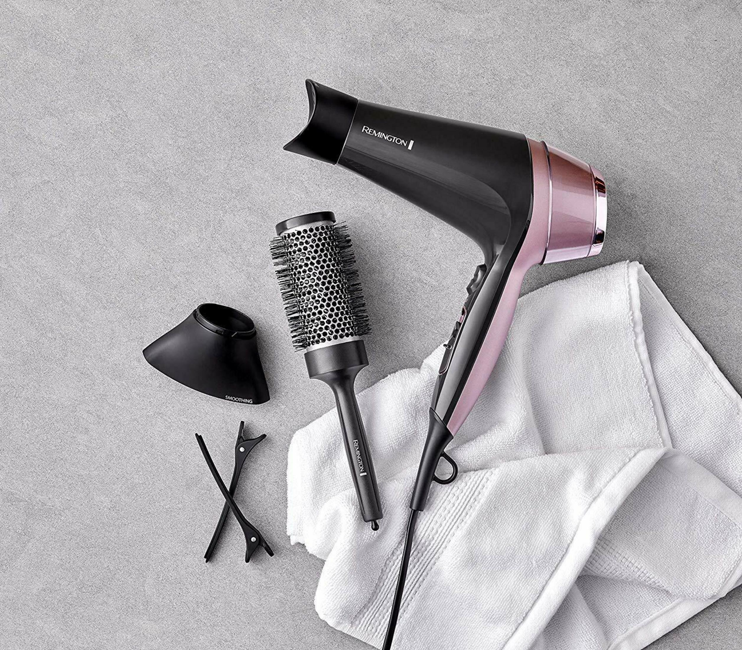 Czarna i różowo-złota suszarka do włosów z akcesoriami na szarym tle.