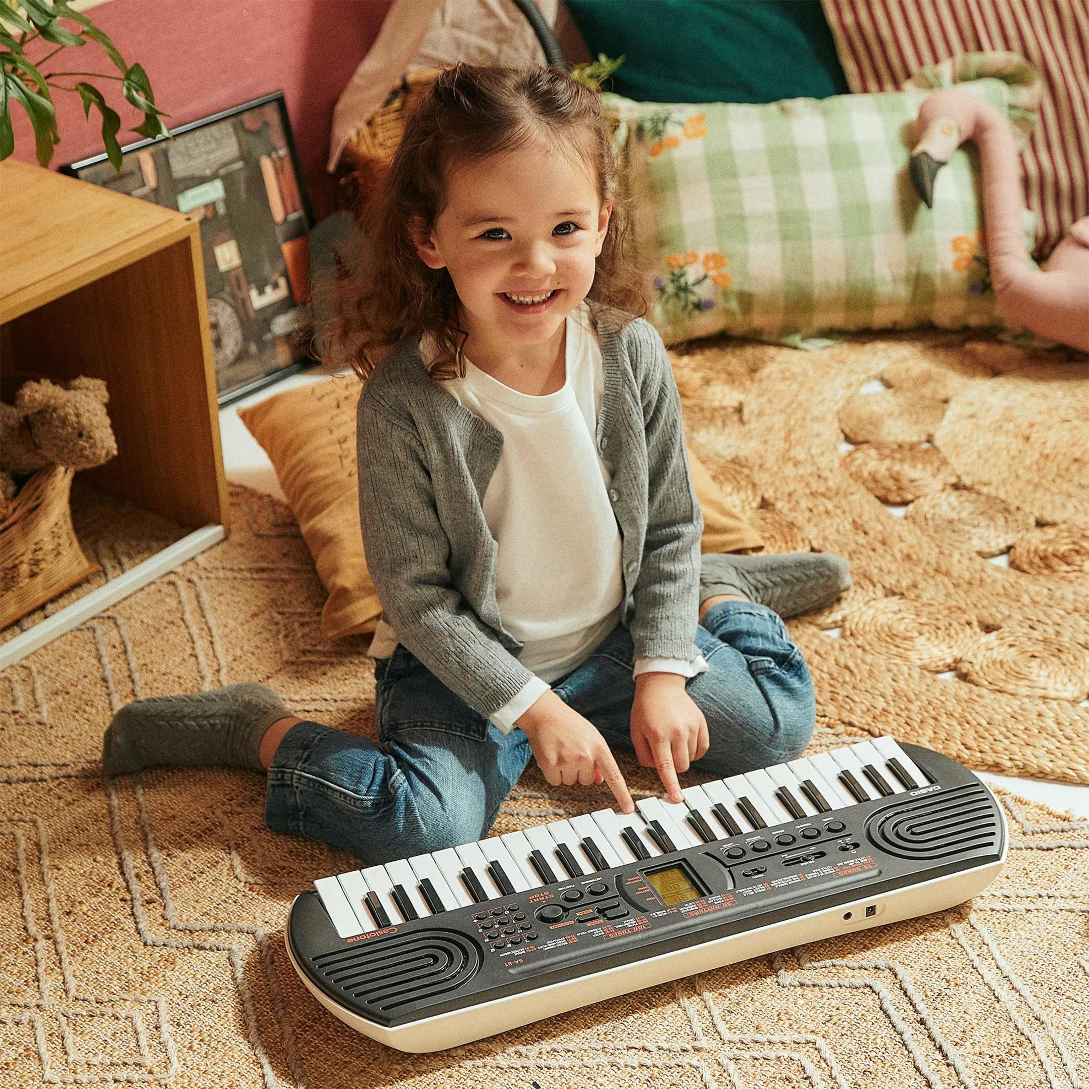 Ein kleines Mädchen mit Locken spielt auf einem Keyboard in einem gemütlichen Raum.