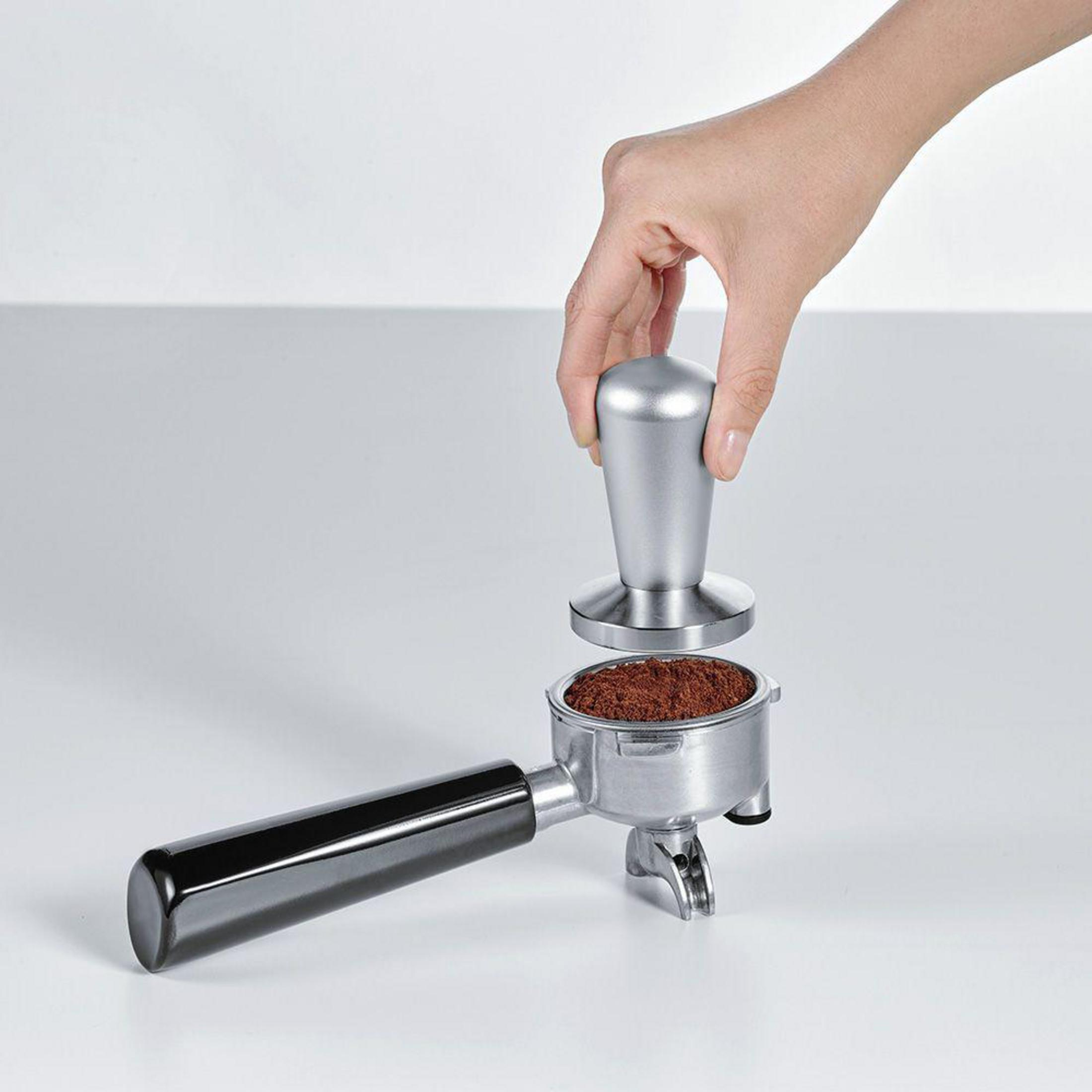 Dłoń trzymająca srebrną tamper nad uchwytem filtra z mieloną kawą.