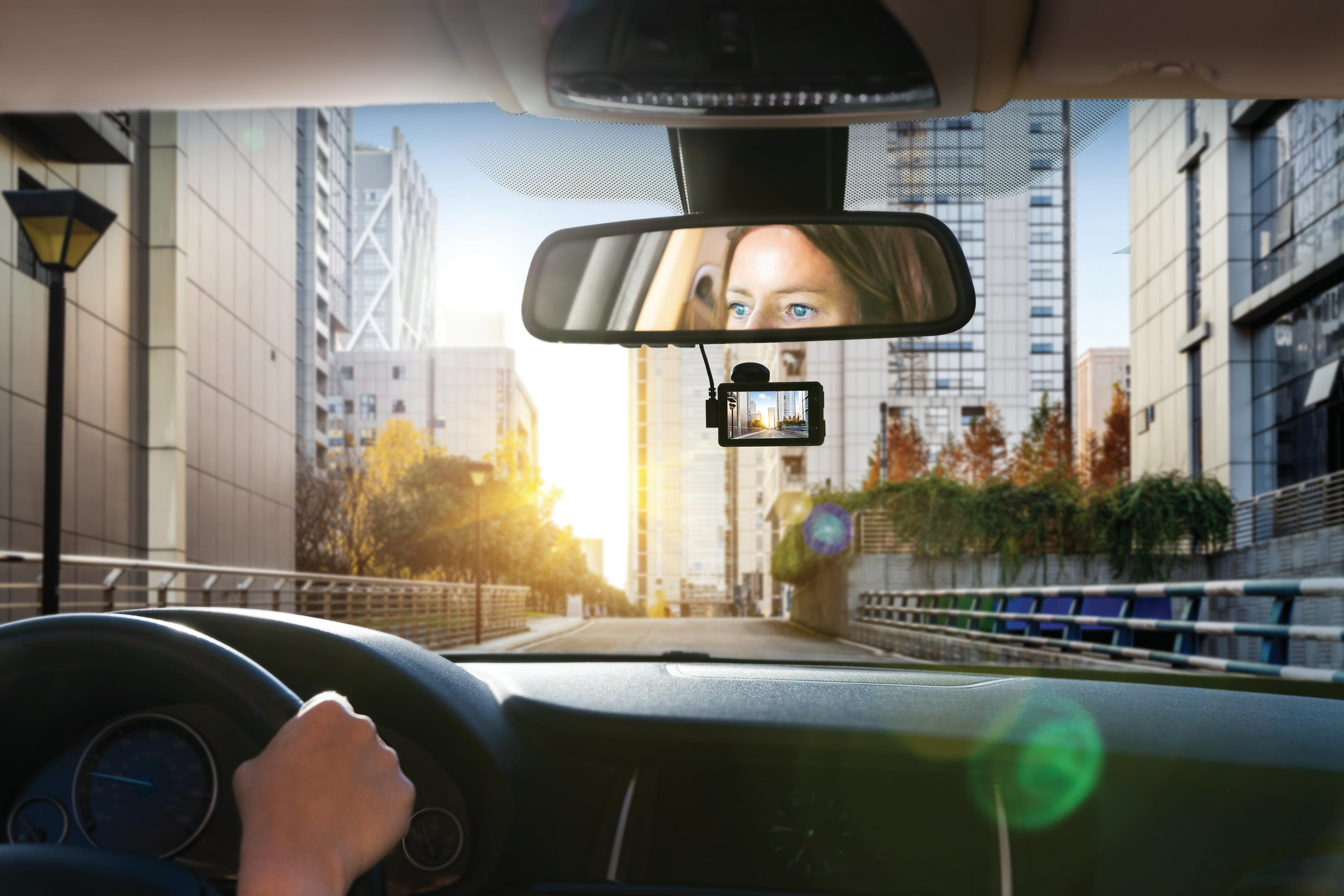 Blick aus Auto: Hand am Lenkrad, Armaturenbrett, Rückspiegel mit Frau, Dashcam, Stadt.