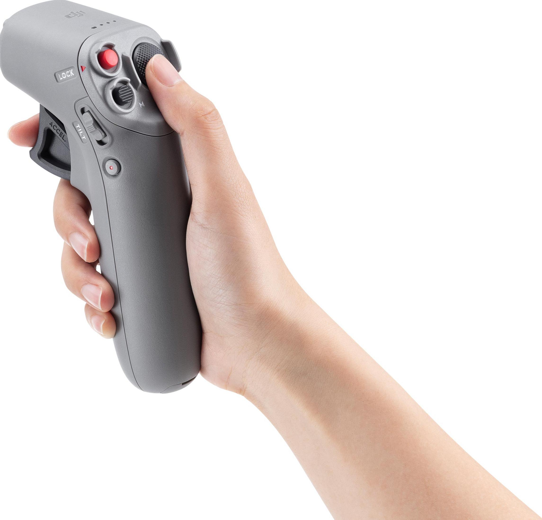 Dłoń trzyma szary kontroler z czerwonymi i czarnymi przyciskami.