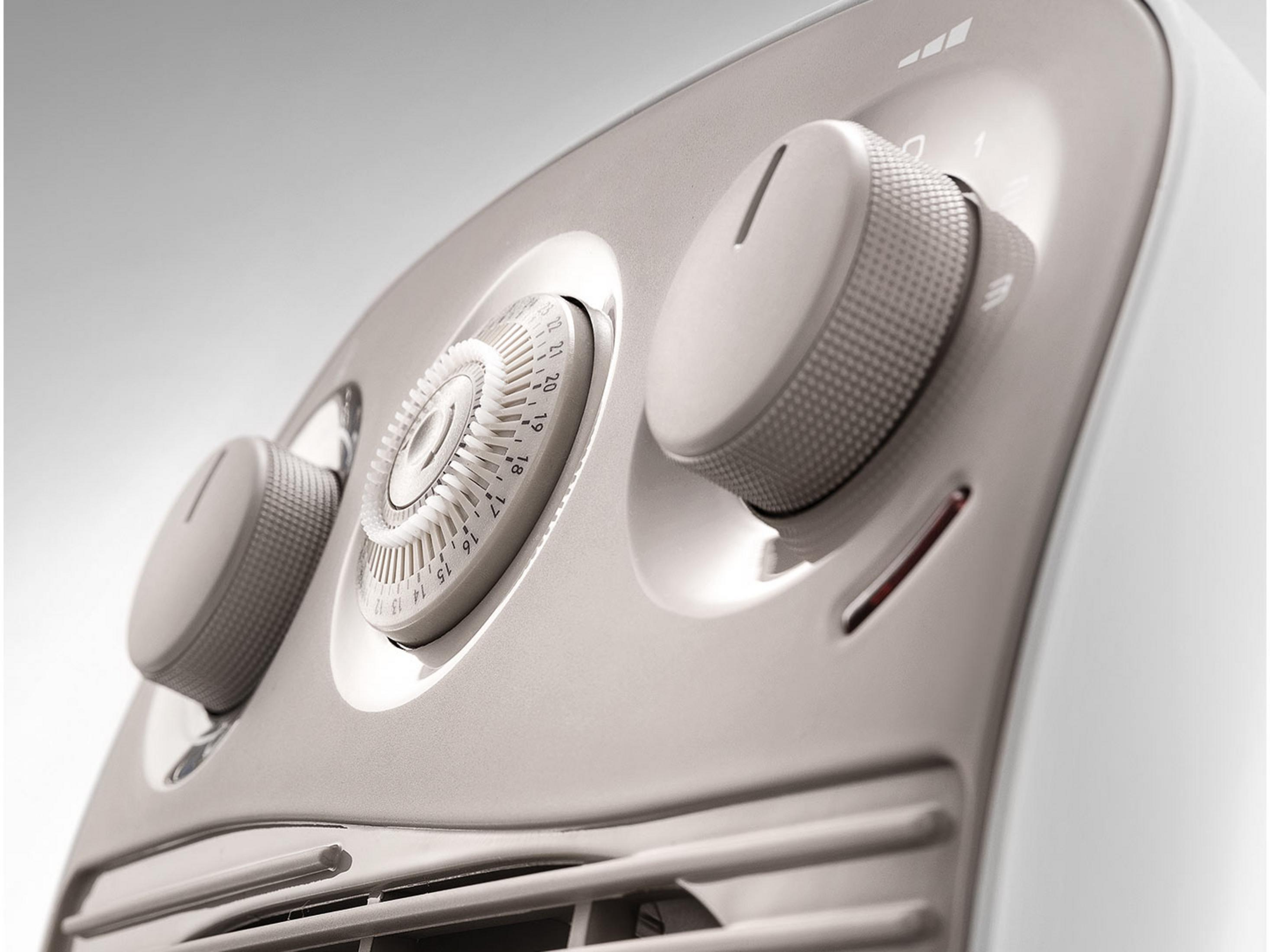 Zbliżenie białego grzejnika z wentylatorem, dwoma pokrętłami i termostatem.