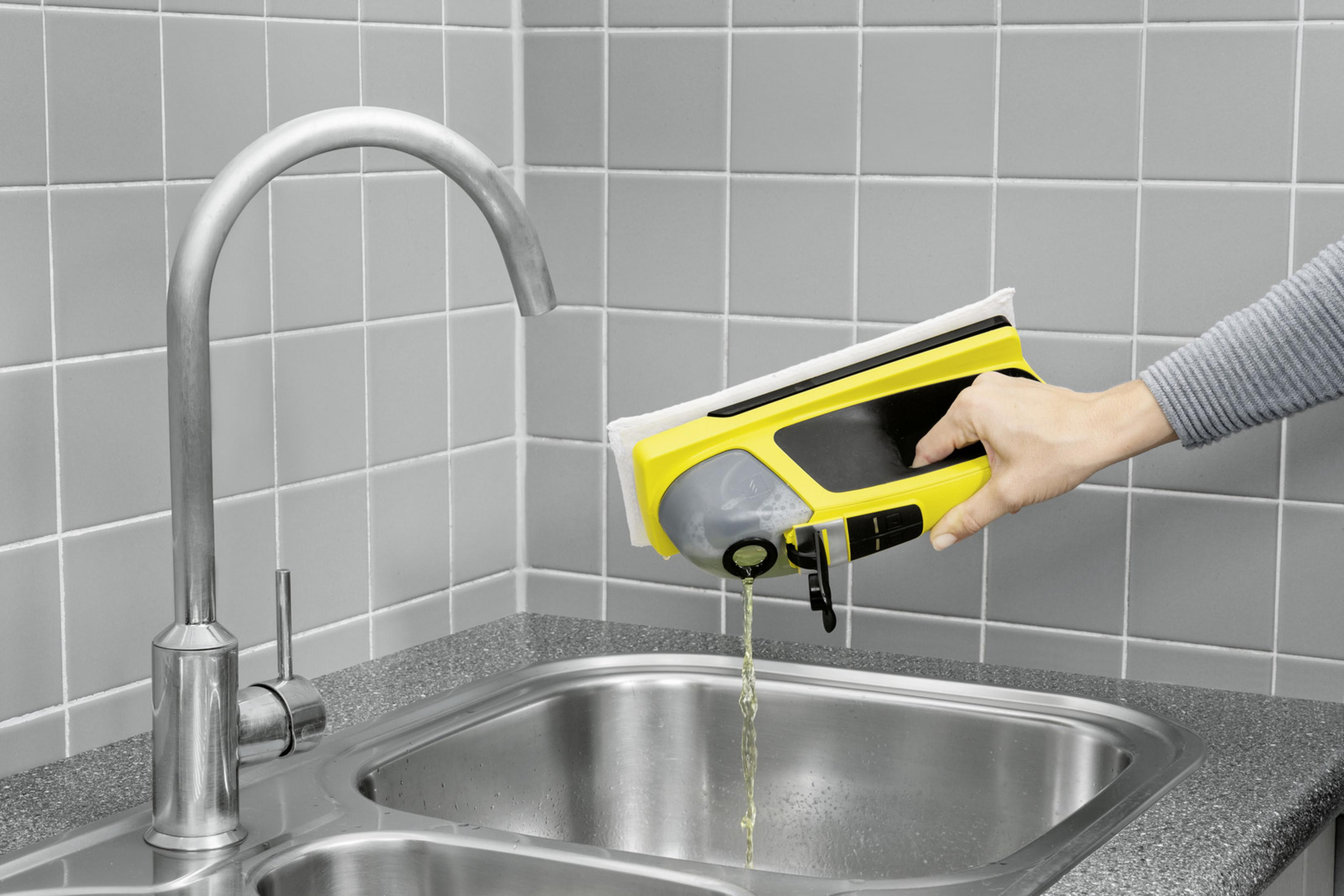 Żółte urządzenie czyszczące opróżnia płyn do zlewu z szarymi płytkami.
