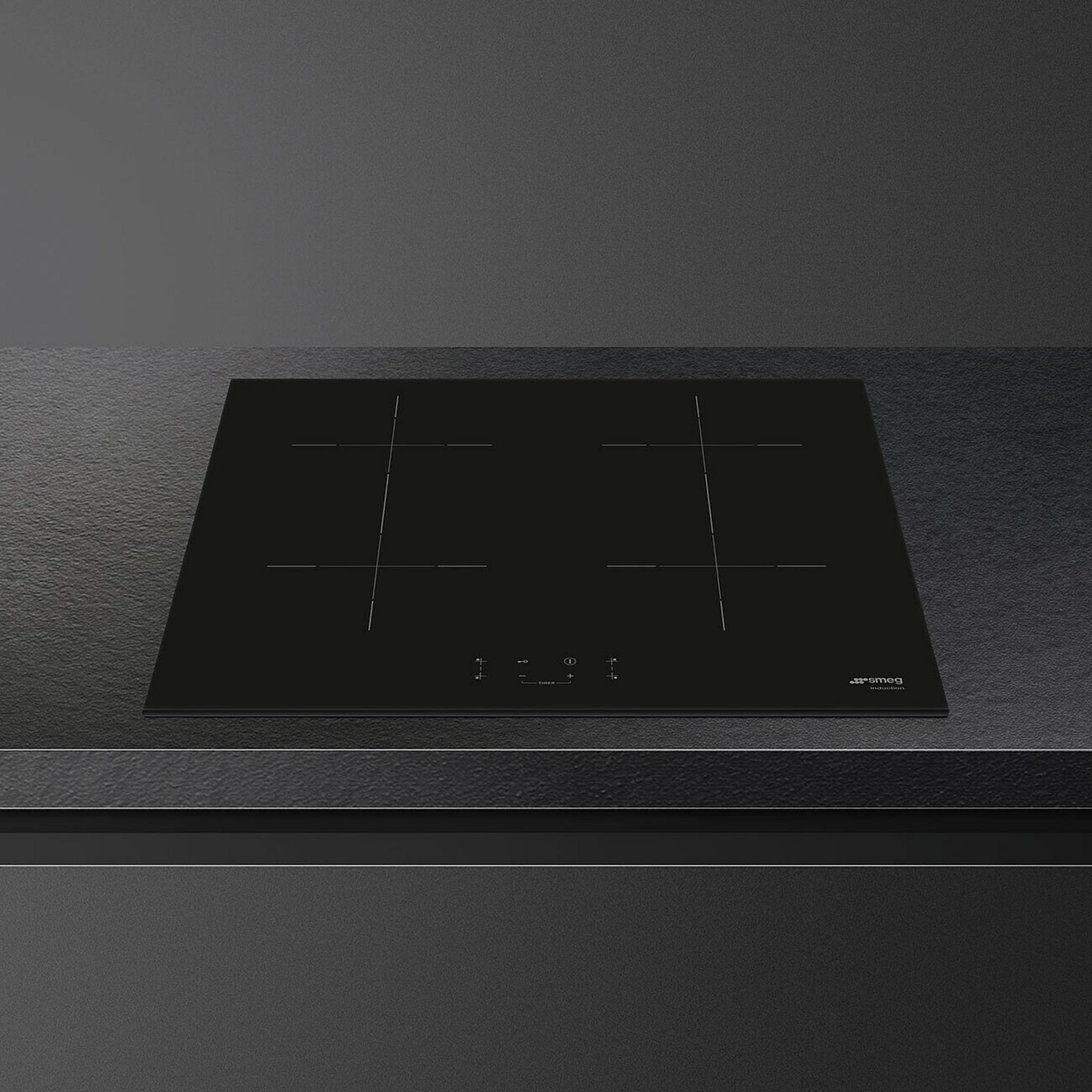 Black induction hob with four cooking zones on a dark countertop.