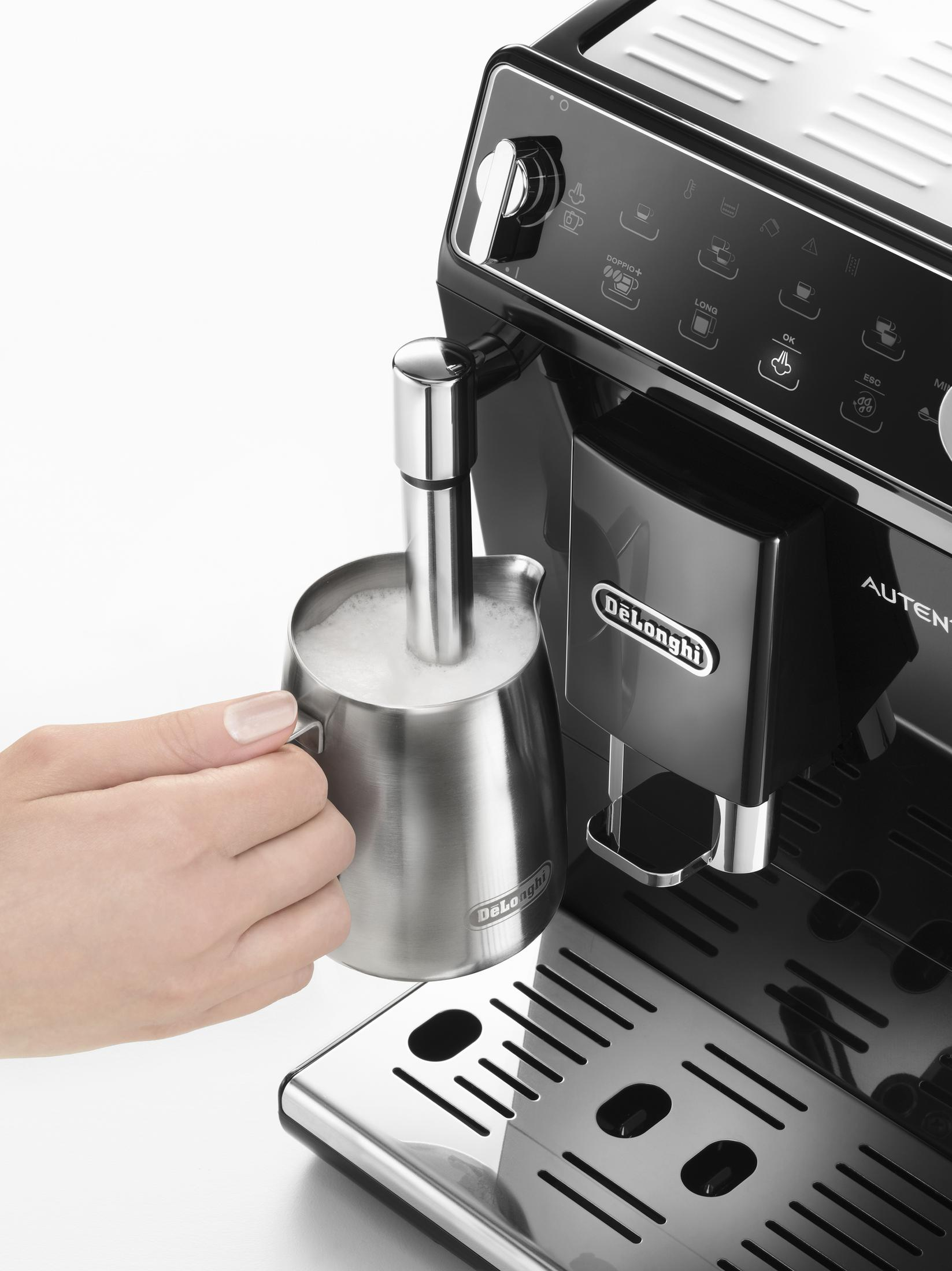 Een hand houdt een metalen kannetje vast terwijl een stoompijpje melk opschuimt.
