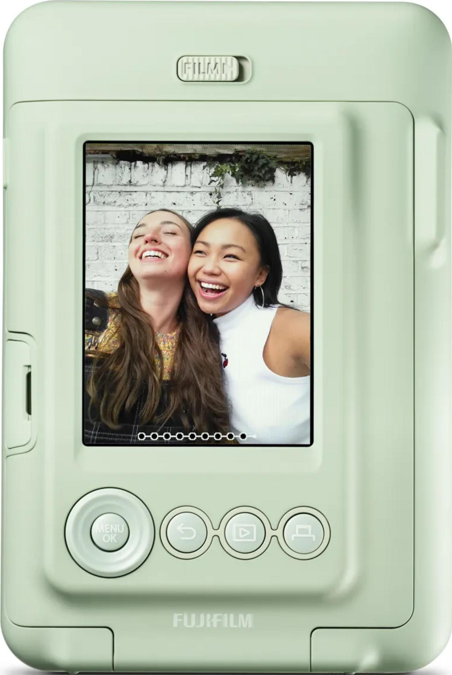 Cámara instantánea Fujifilm verde claro mostrando a dos mujeres jóvenes riendo posando para una selfie.