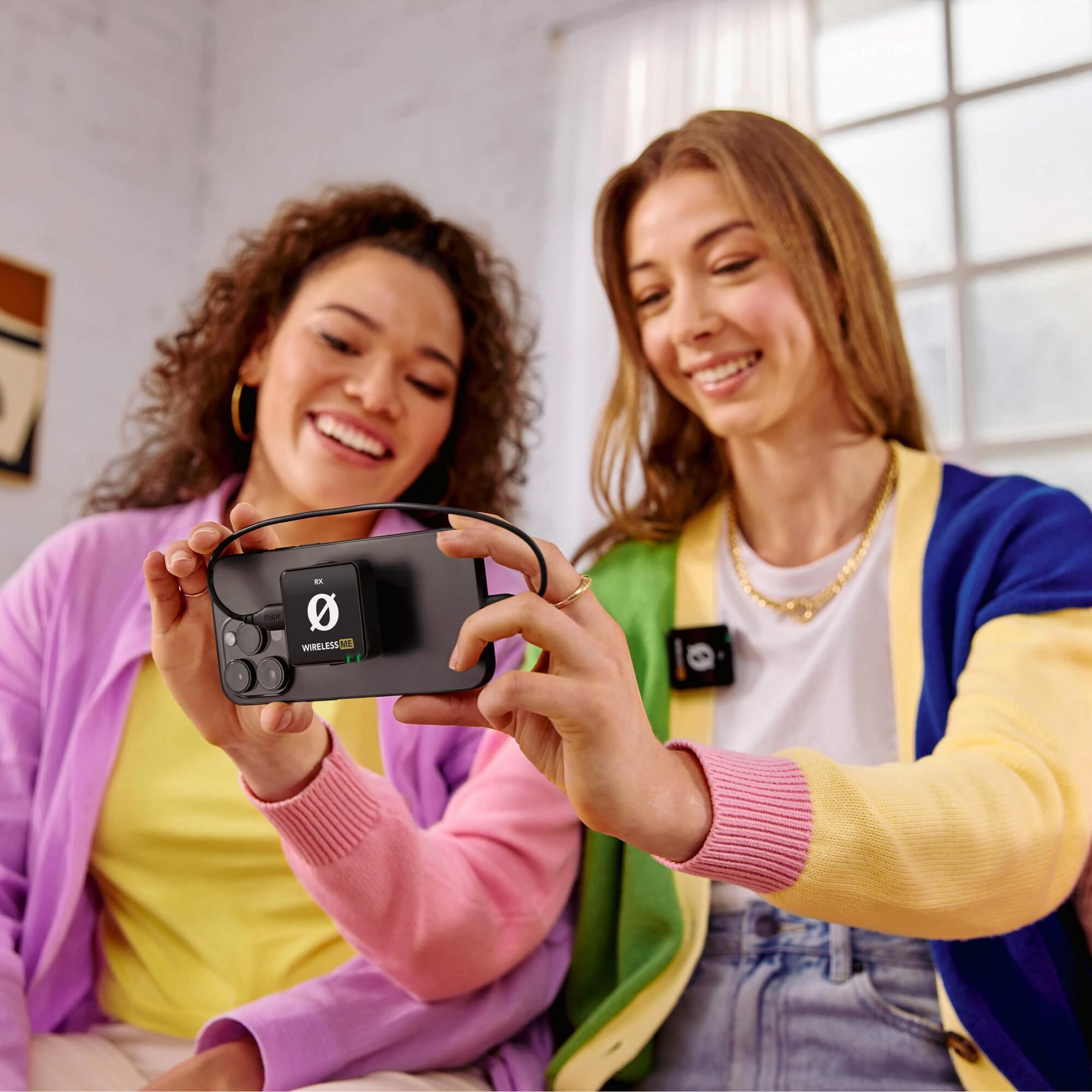 Dwie kobiety trzymają smartfon podłączony do mikrofonu. Uśmiechają się.