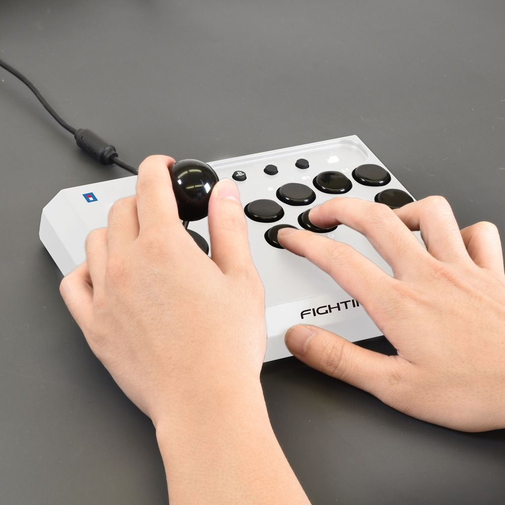 Biały joystick z czarnymi przyciskami i drążkiem, ręce go obsługują.