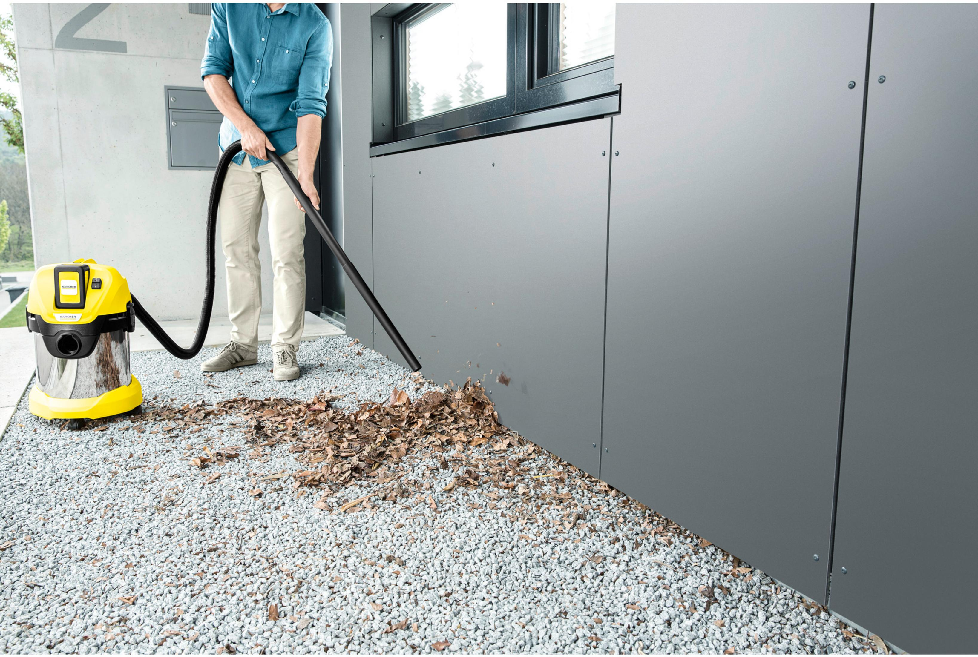 Homme aspirateur feuilles avec aspirateur jaune sur gravier près mur gris.