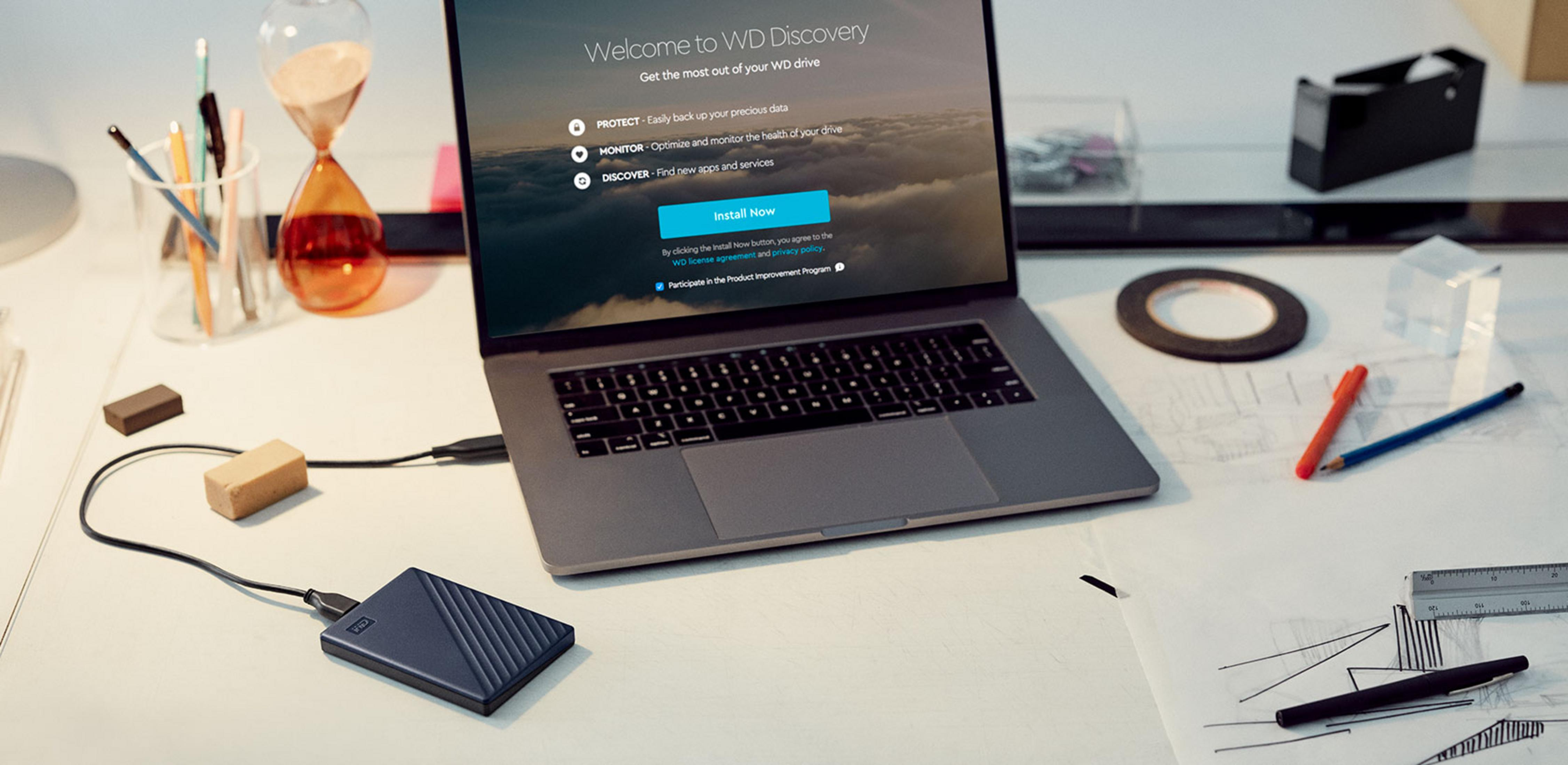 Laptop i zewnętrzny dysk twardy na biurku z artykułami biurowymi.