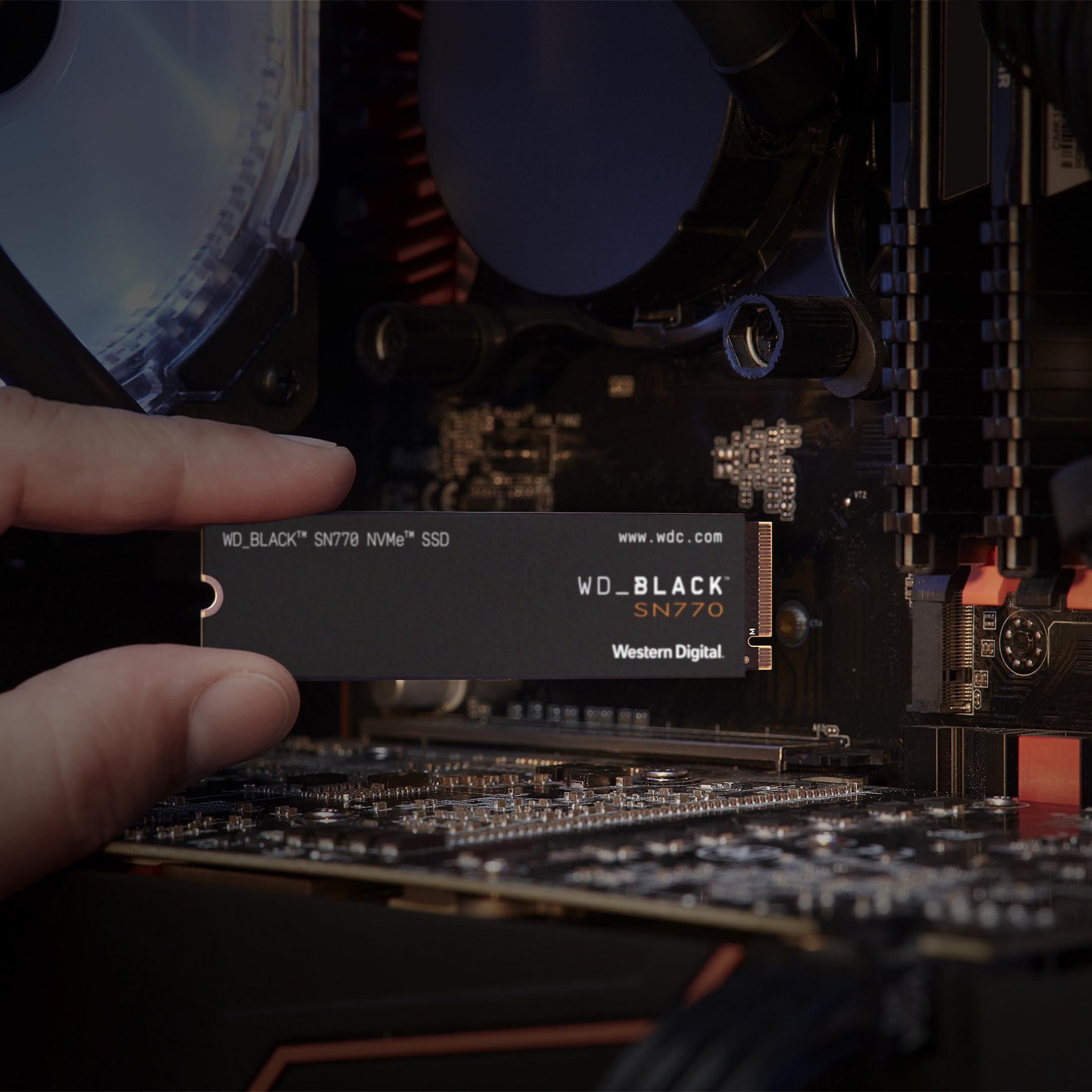 Une main tient un SSD NVMe WD_BLACK SN770 au-dessus d'une carte mère d'ordinateur.